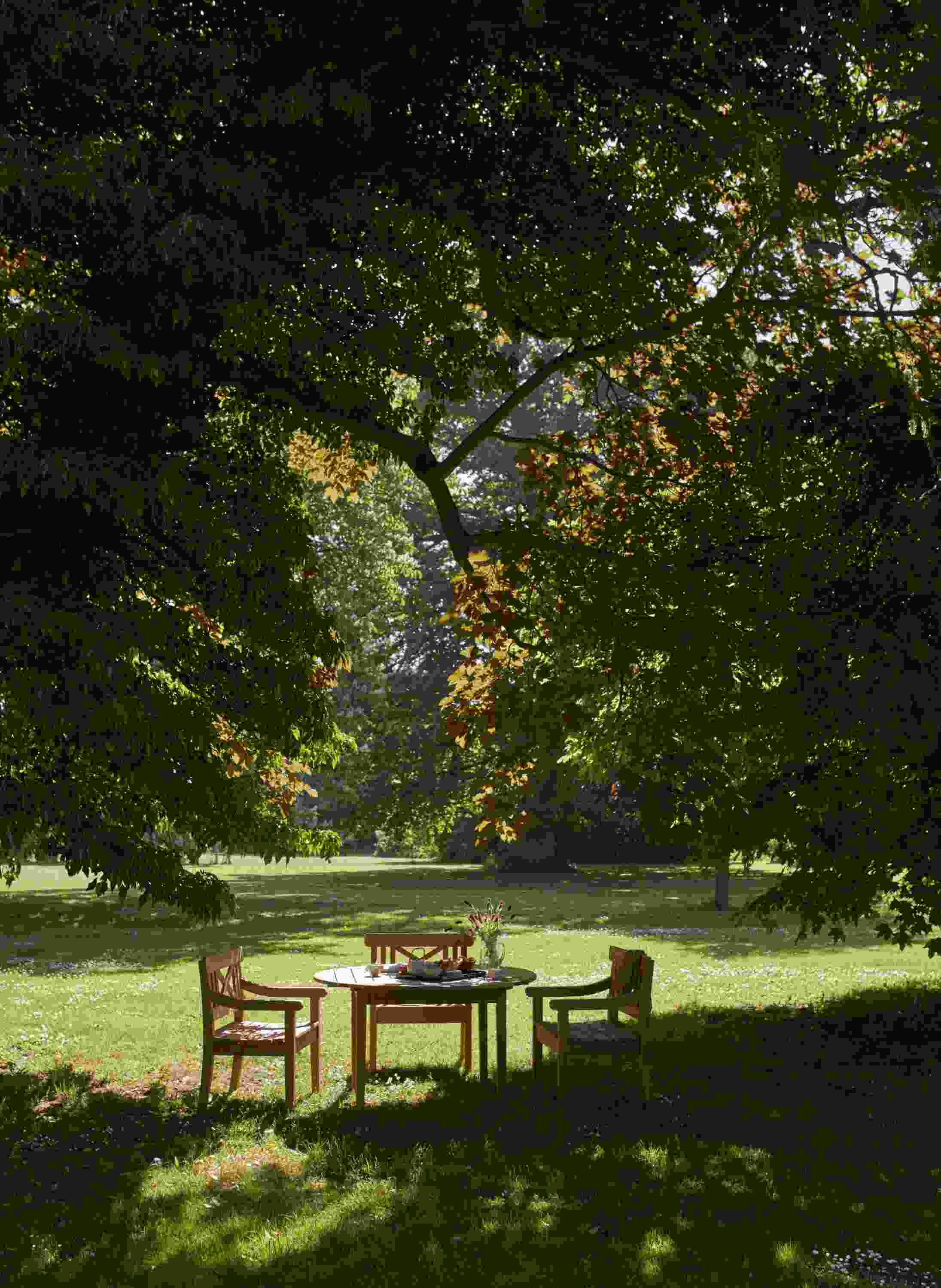 Drachmann Stuhl und Gartentisch von Skagerak by Fritz Hansen unter einem Baum im Garten.