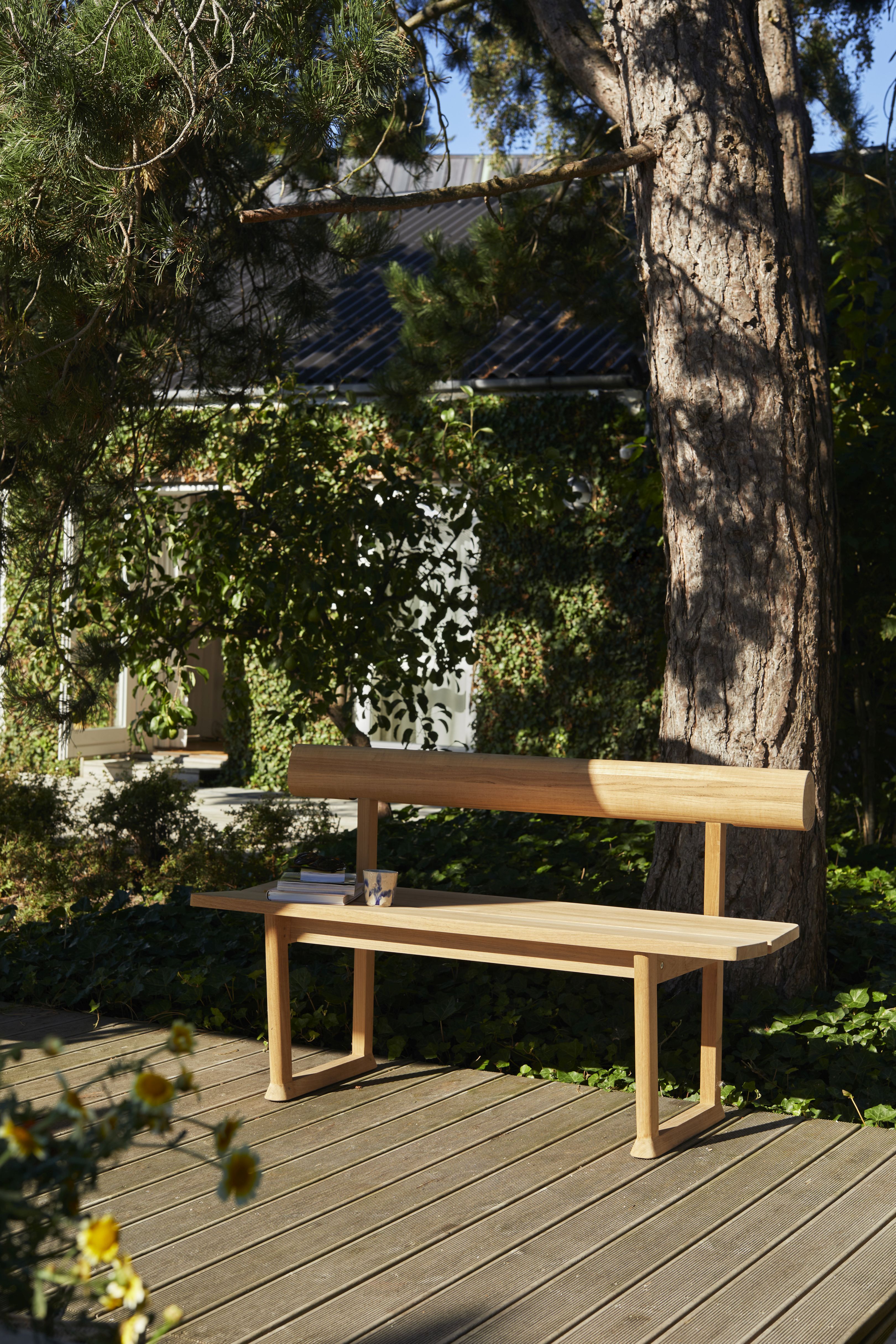 Banco Bank Teak Outdoor von Skagerak by Fritz Hansen im Garten auf Holzterrasse, Bücher und Tasse.