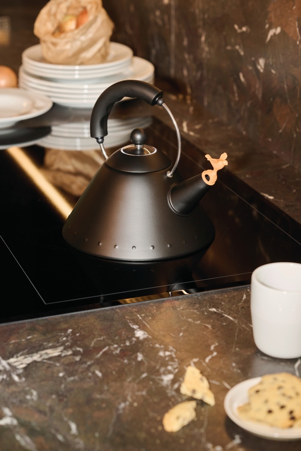 Schwarzer 9093 BB Wasserkessel von Alessi auf einem Induktionskochfeld mit Vogelpfeife und Teetasse.