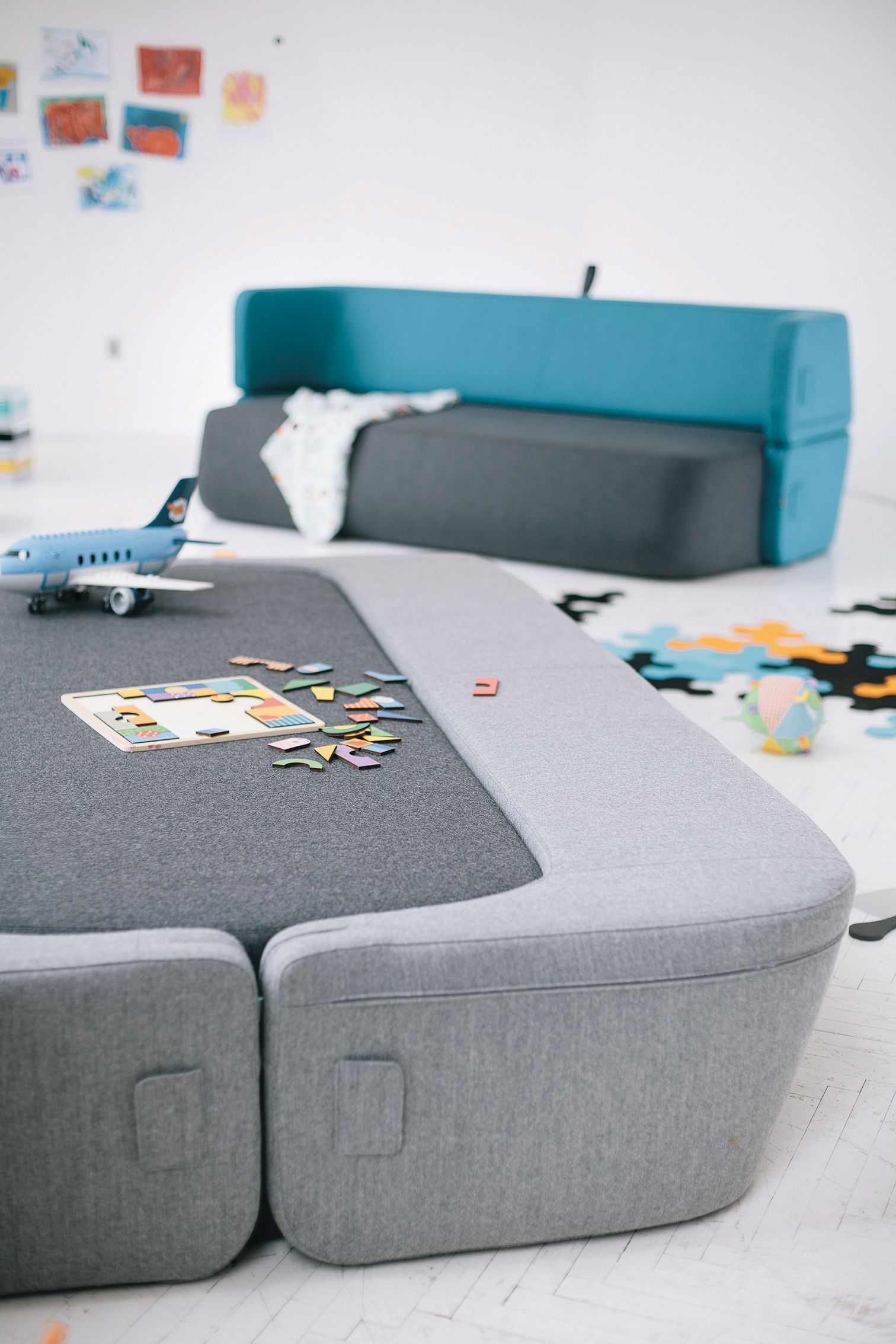 Graues Revolve Schlafsofa von Prostoria im Kinderzimmer mit Spielzeug und Puzzle.