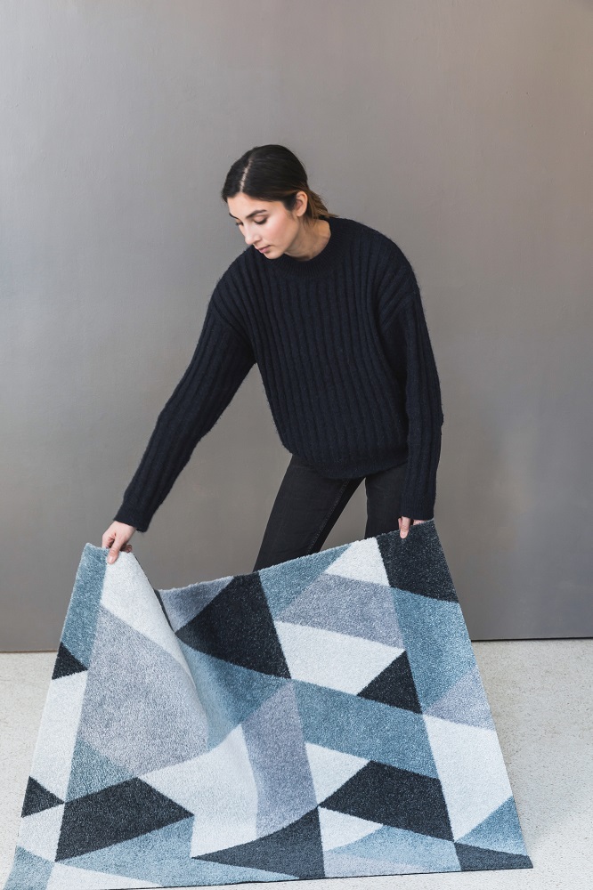 Frau rollt blaue Blåne Heymat Fußmatte mit geometrischem Muster aus, Indoor und Outdoor geeignet.