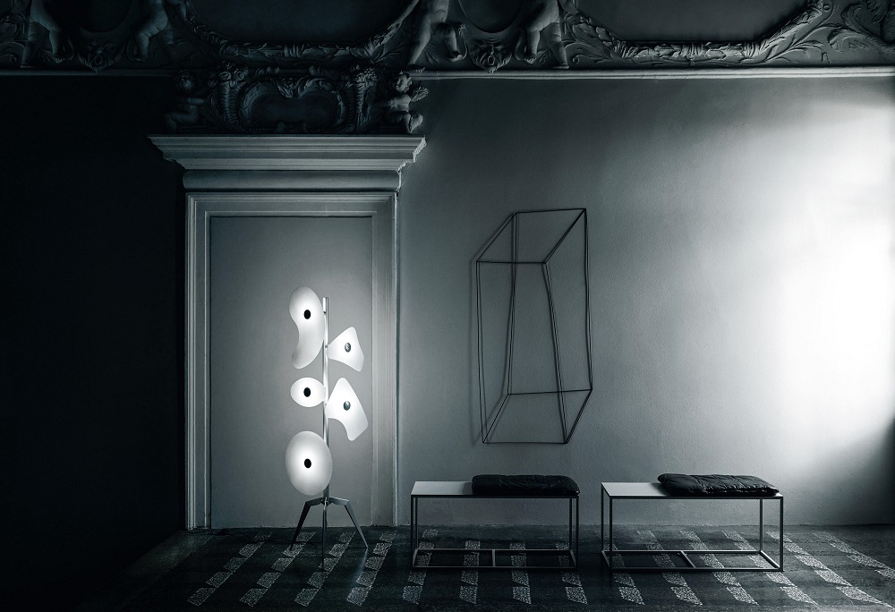 Moderne Stehlampe mit fünf Leuchten in Weiß, minimalistische Bänke und Drahtkunst an grauer Wand.