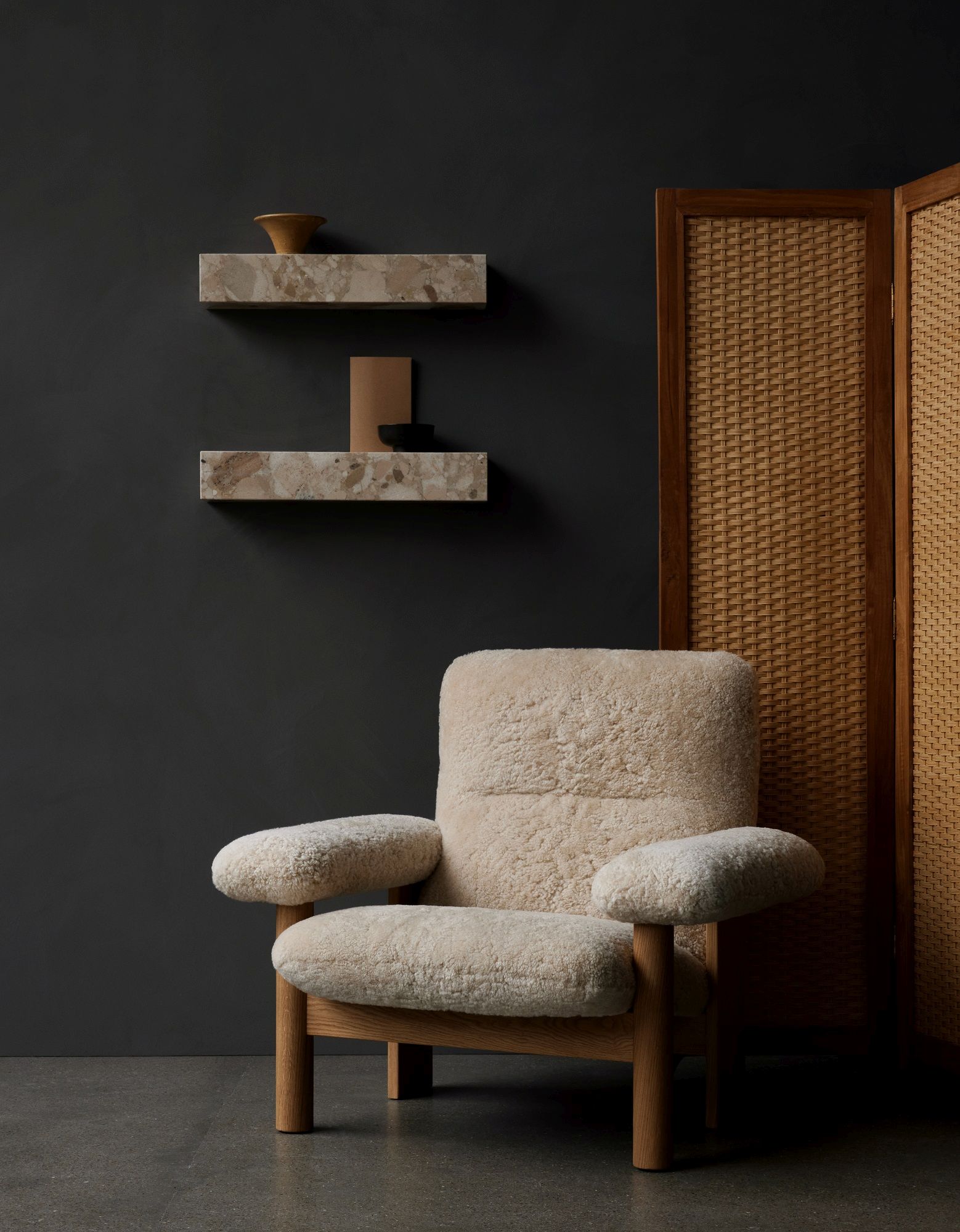 Audo Copenhagen Plinth Shelf Regale aus Marmor über einem Sessel mit Schaffellbezug und Raumteiler.