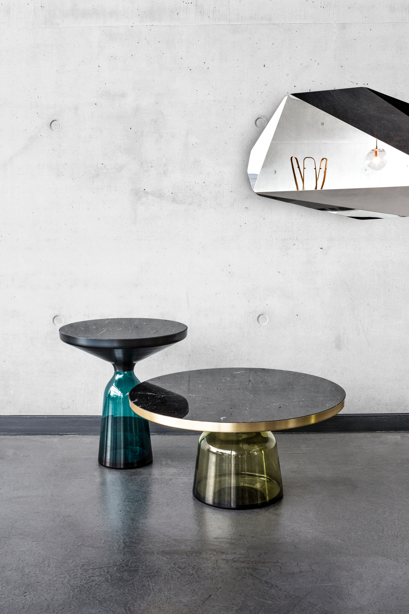 Zwei ClassiCon Bell Side Tables mit Marmor Tischplatte und farbigem Glasfuß vor Betonwand.