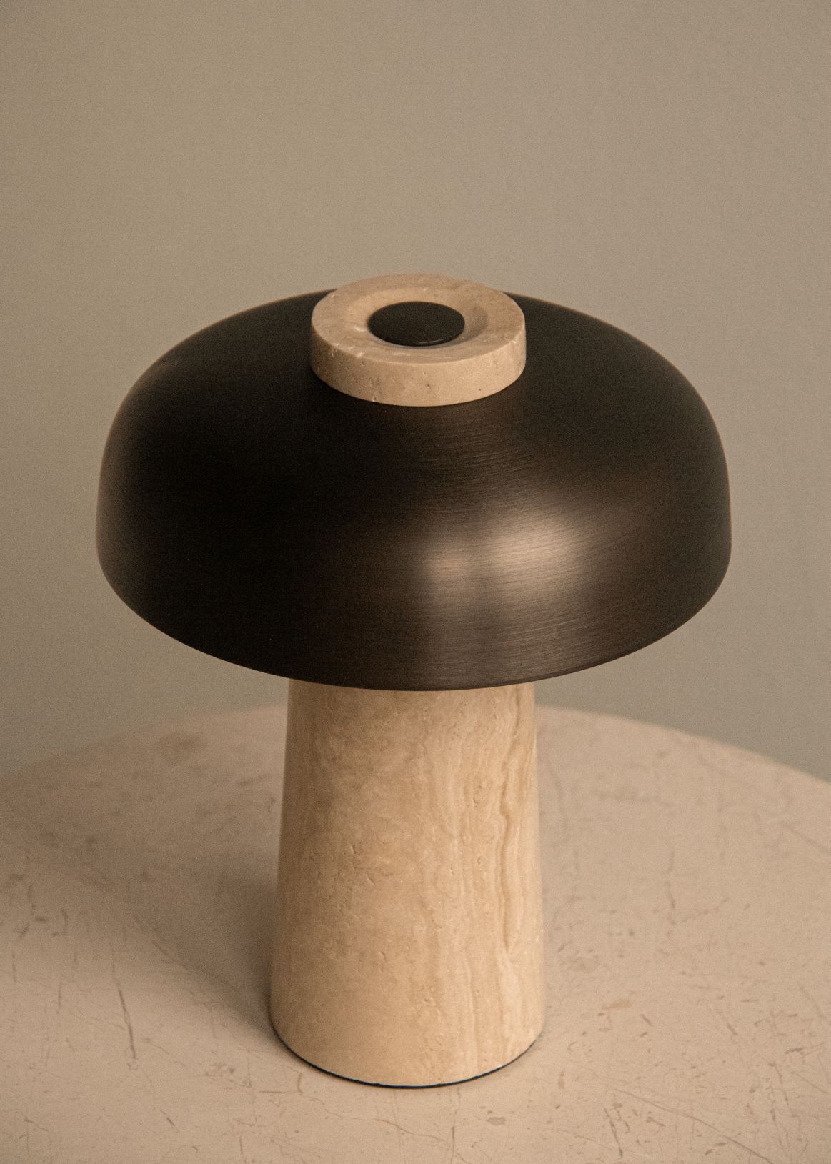 Audo Copenhagen Reverse Akkuleuchte aus Travertin und brüniertem Aluminium auf einem Tisch.