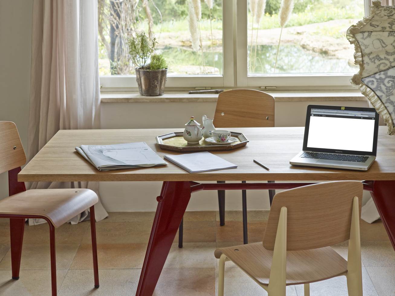 Vitra EM Table Holztisch mit rotem Untergestell, Büromaterialien und Laptop in einem hellen Raum.