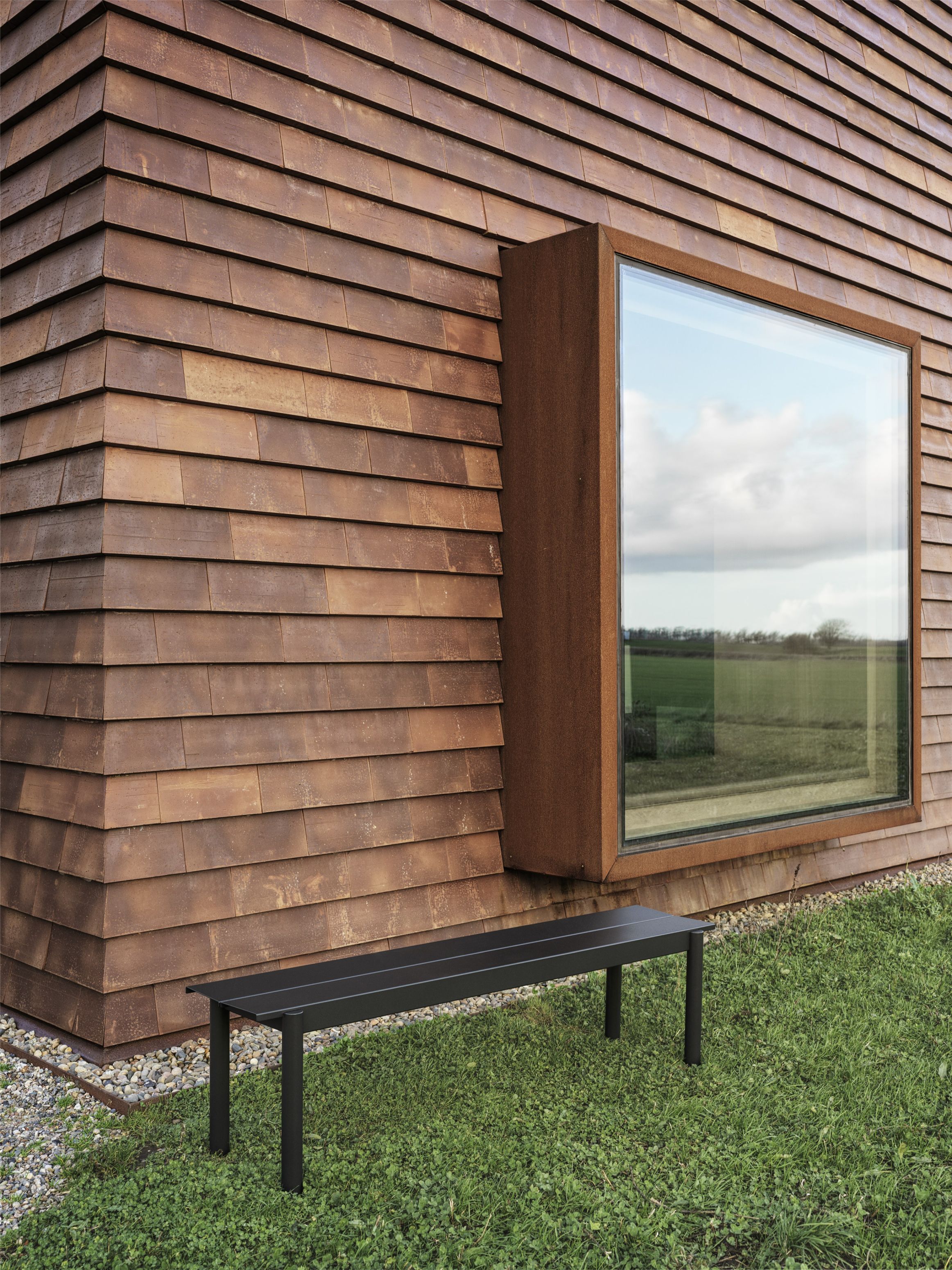 Muuto Linear Steel Bench Outdoor Bank in Schwarz vor modernem Haus mit Holzfassade.