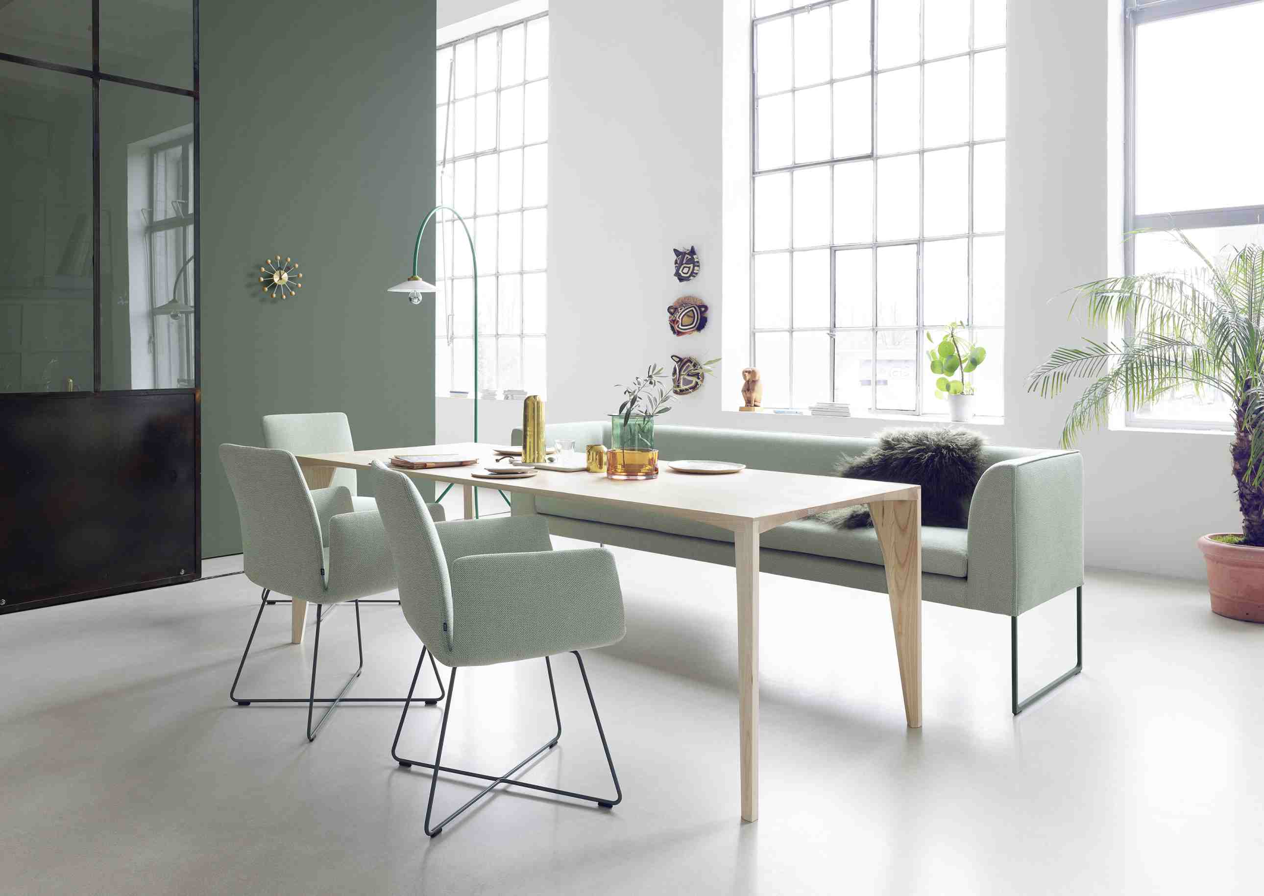 Helles Esszimmer mit Esstisch aus Holz, grüner Sitzbank und Stühlen mit schwarzem Gestell.