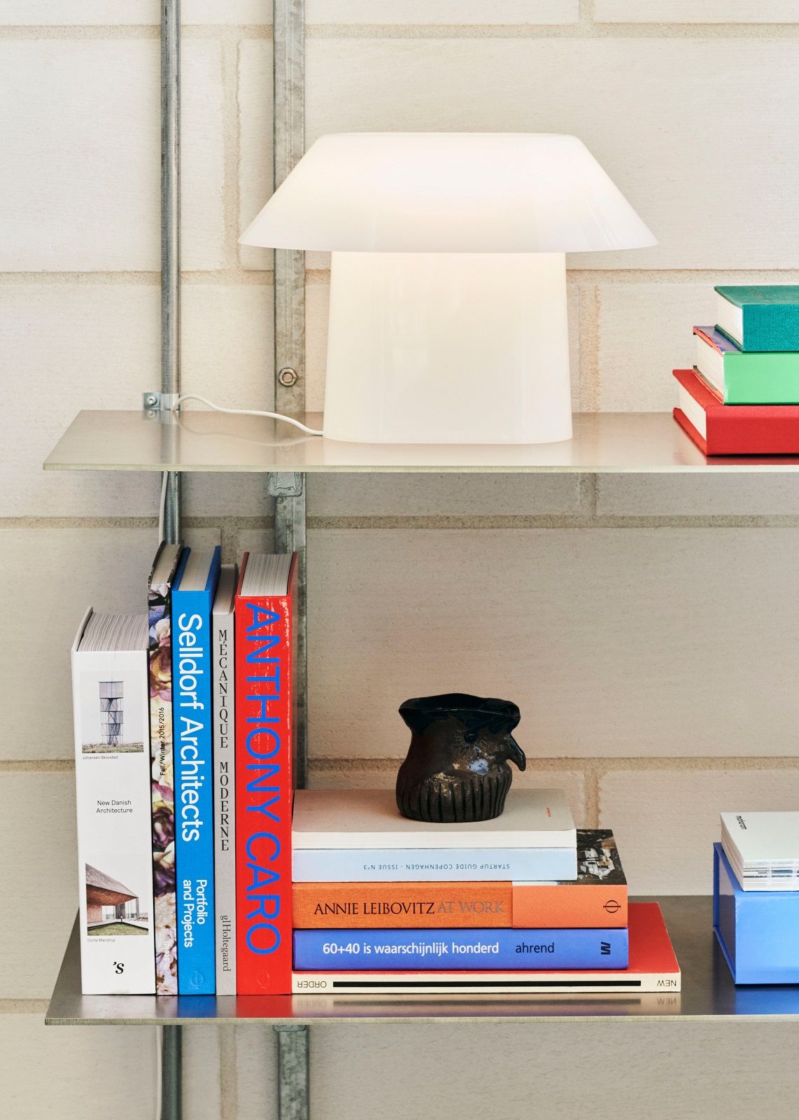 Helle, moderne Drome Tischleuchte von Hay auf einem Regal mit Büchern und Dekoration.