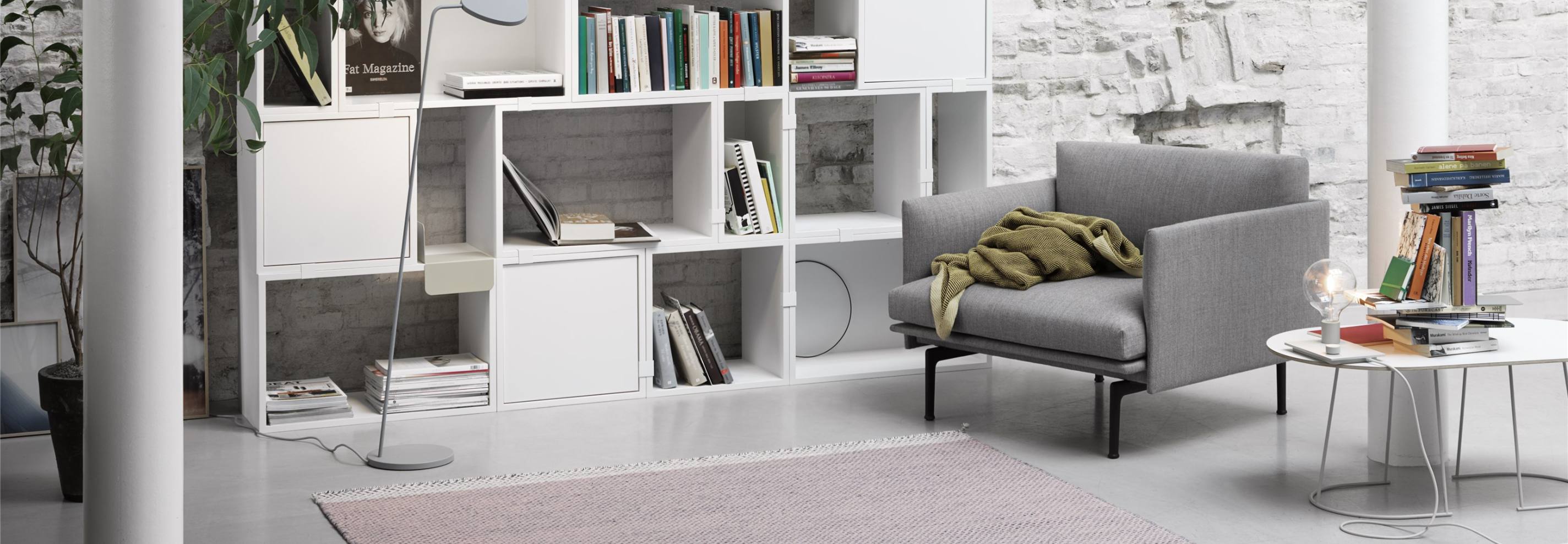 Grauer Sessel mit Decke, weißes Bücherregal, Beistelltisch mit Lampe und Büchern, modernes Wohnzimmer Interieur.