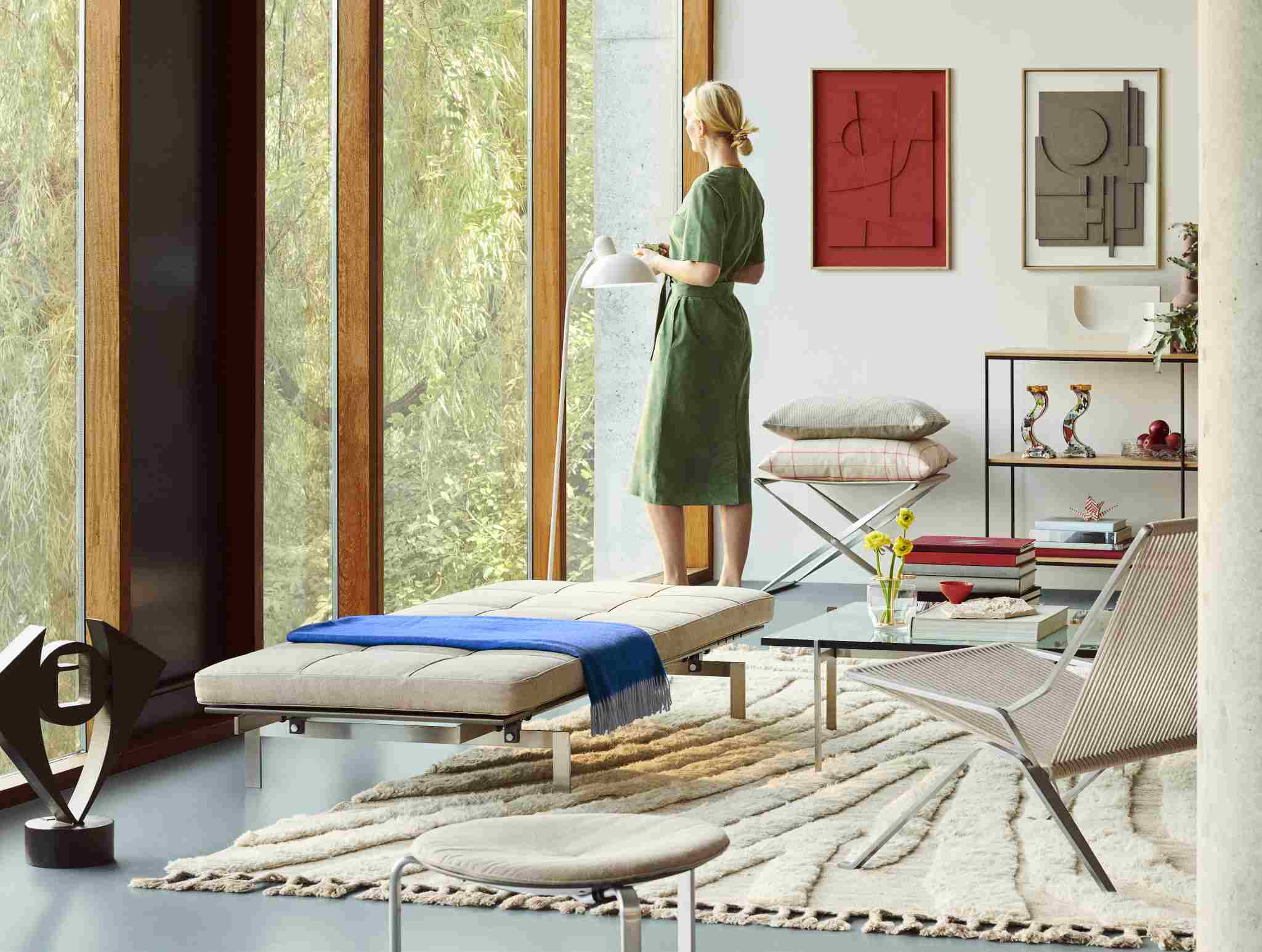 Helle, moderne Inneneinrichtung mit Fritz Hansen PK80 Liege, Teppich und Frau am Fenster.