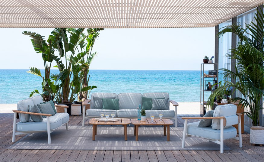 Emu Twins Sofa Outdoor-Lounge-Set auf Holzterrasse mit Meerblick, bestehend aus Sofa, Sessel und Couchtischen.