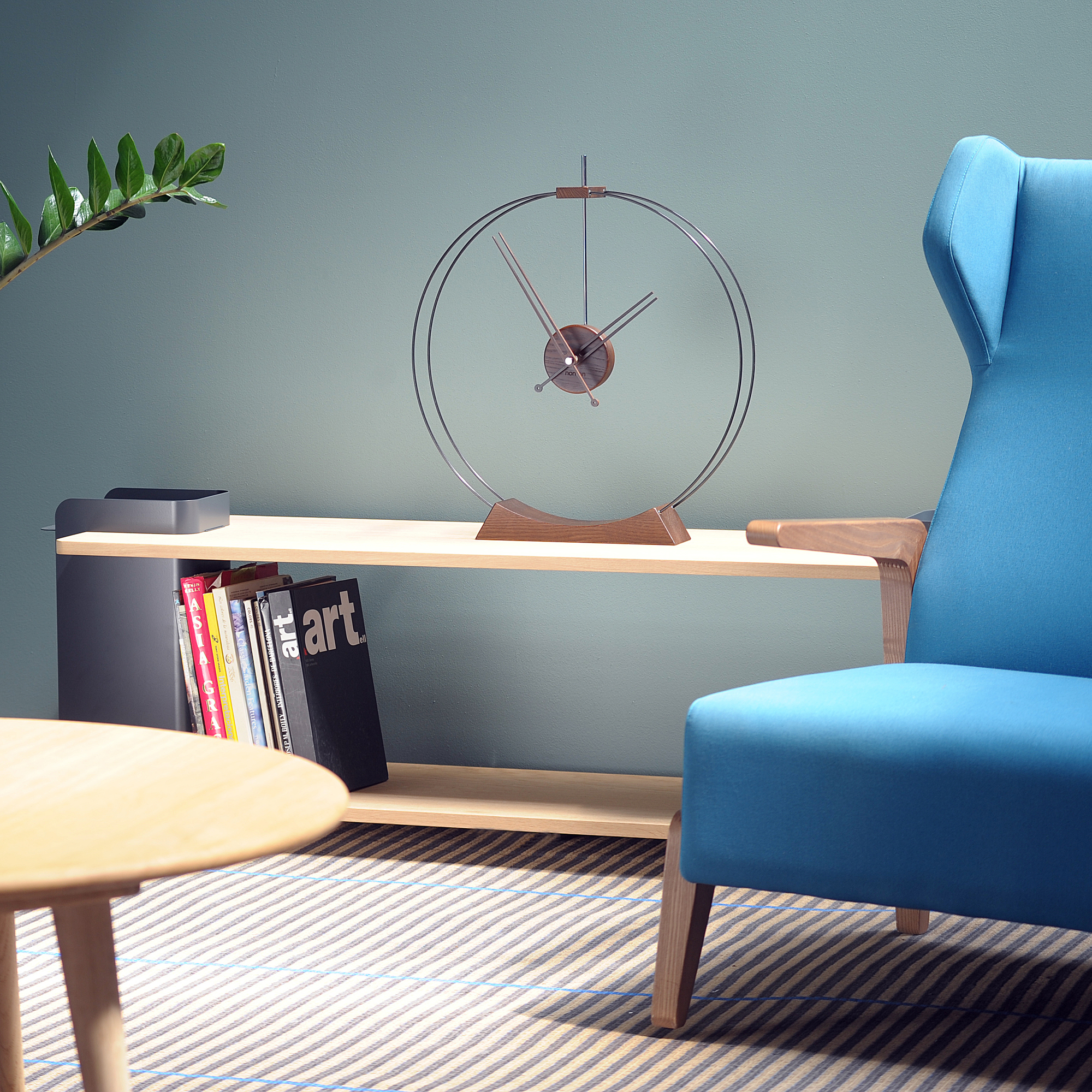 Aire Tischuhr von Nomon auf einem Regal, minimalistisches Design mit Holzfuß und Metallring.