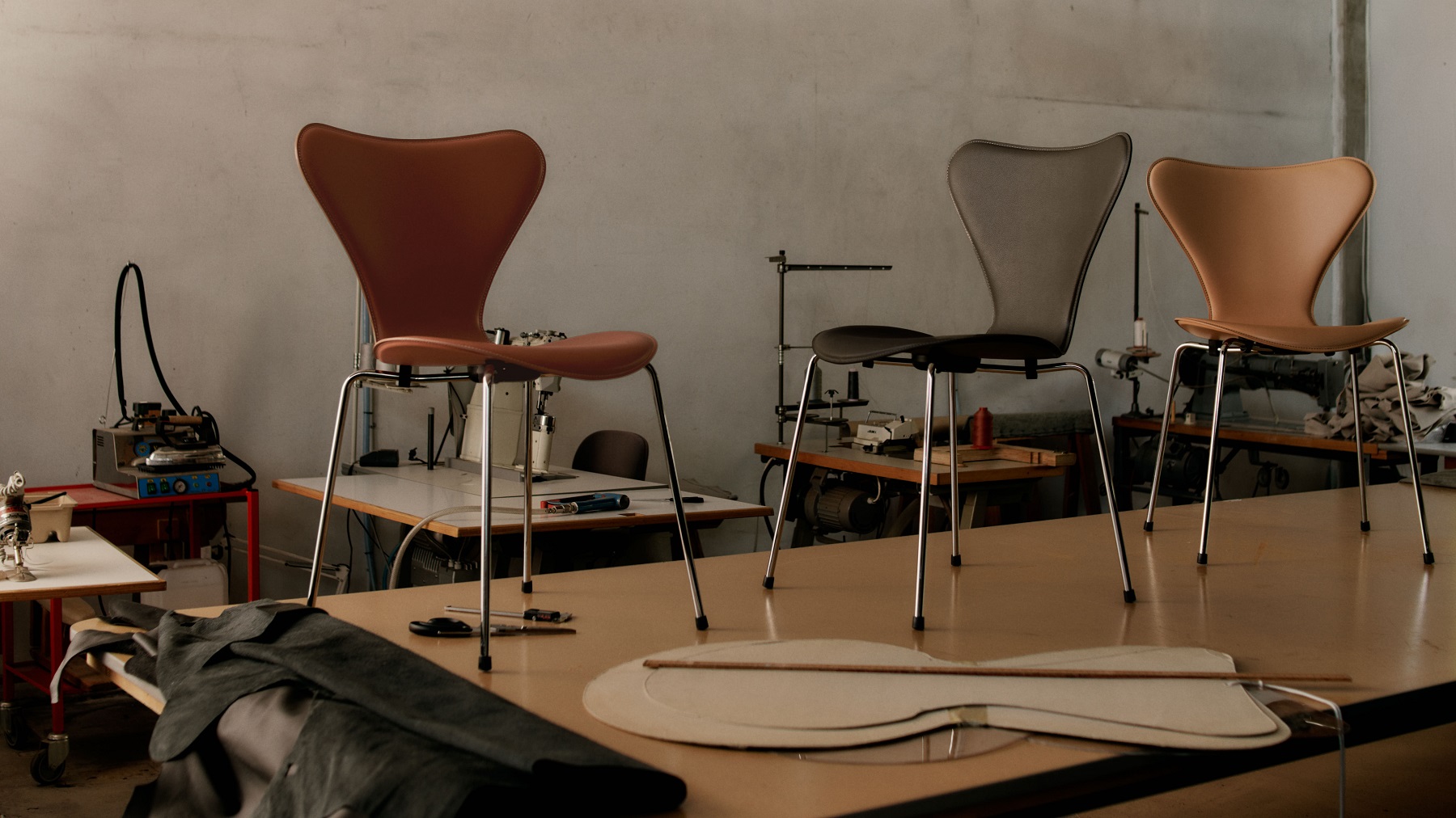 Drei Siebener Stühle von Fritz Hansen in verschiedenen Farben in einer Werkstatt mit Nähmaschinen.