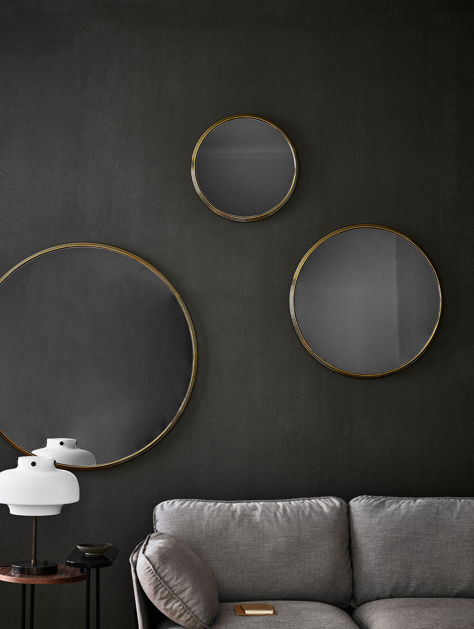 Graues Cloud 2-Sitzer Sofa von AndTradition mit runden Spiegeln und Lampe vor dunkler Wand.