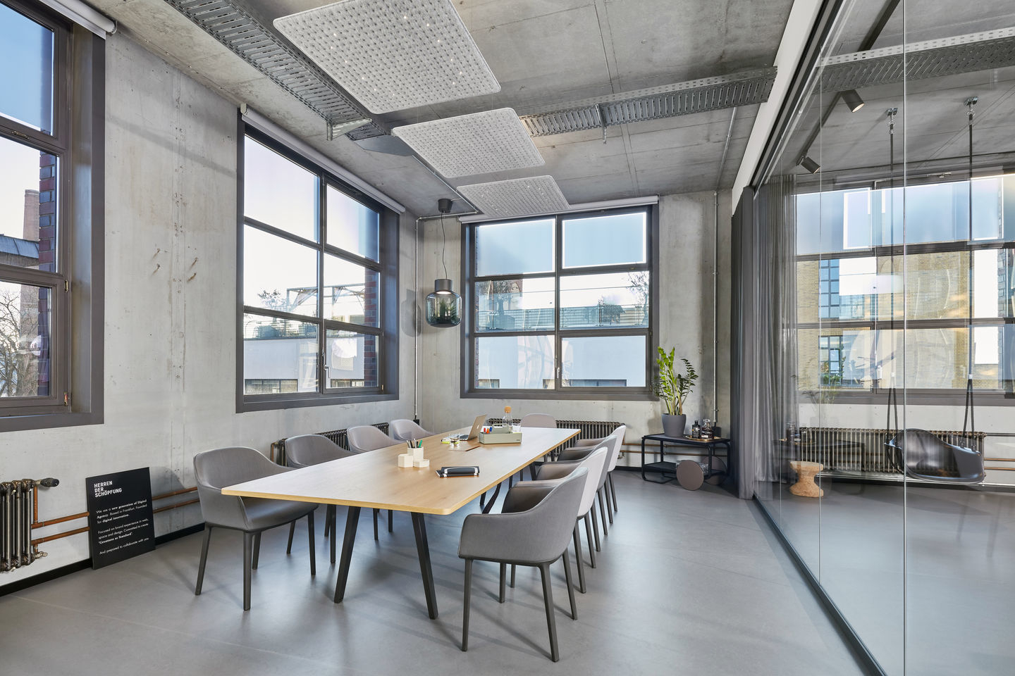 Konferenzraum mit großem Holztisch und mehreren grauen Vitra Softshell Chairs mit Vierbein-Fußgestell.