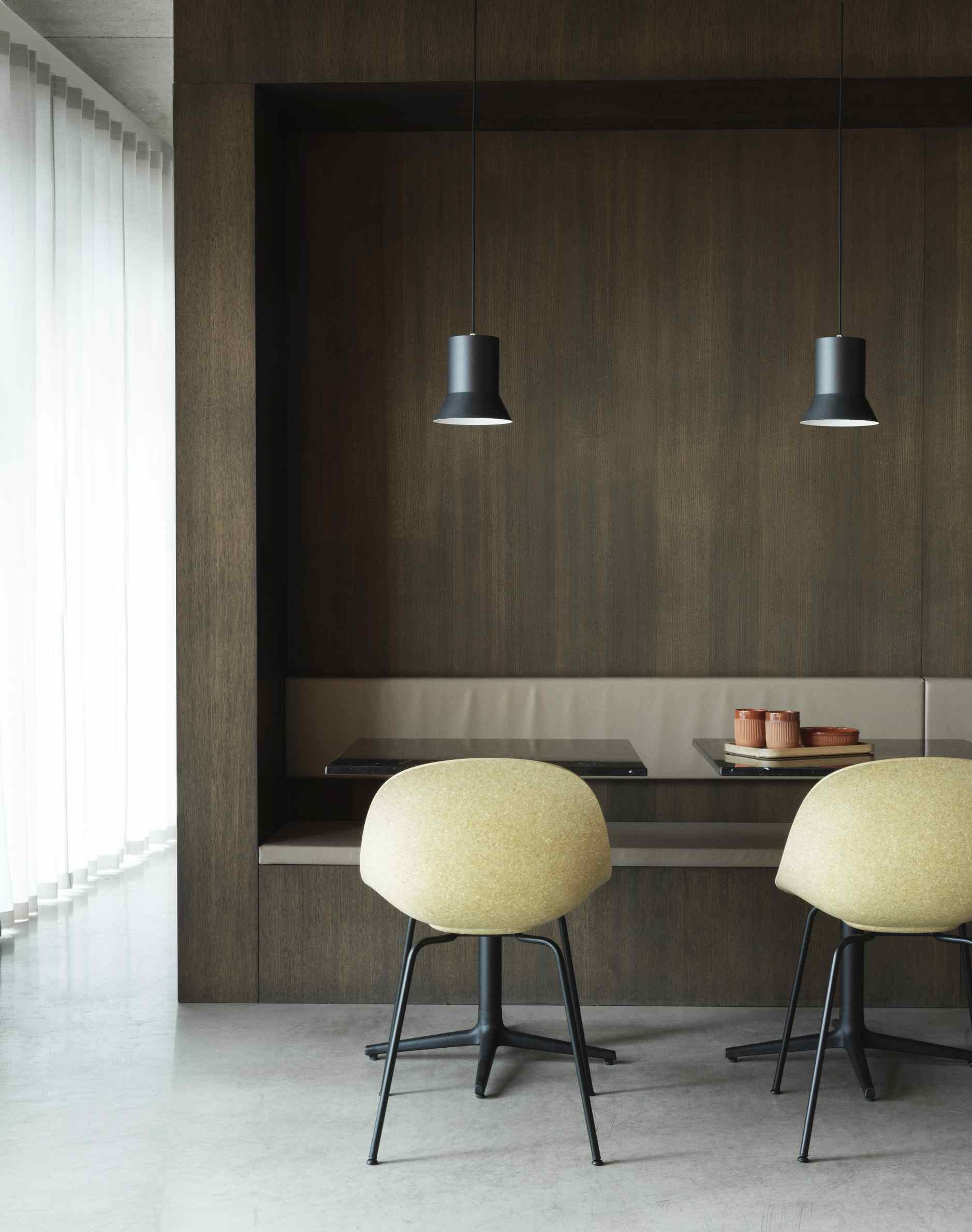 Zwei Mat Chair Steel Stühle von Normann Copenhagen in gelb vor dunkler Holzwand mit Sitzbank.