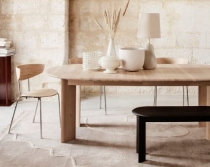 Heller Esstisch aus Holz mit Stühlen und Bank, dekoriert mit Vasen und Lampe.