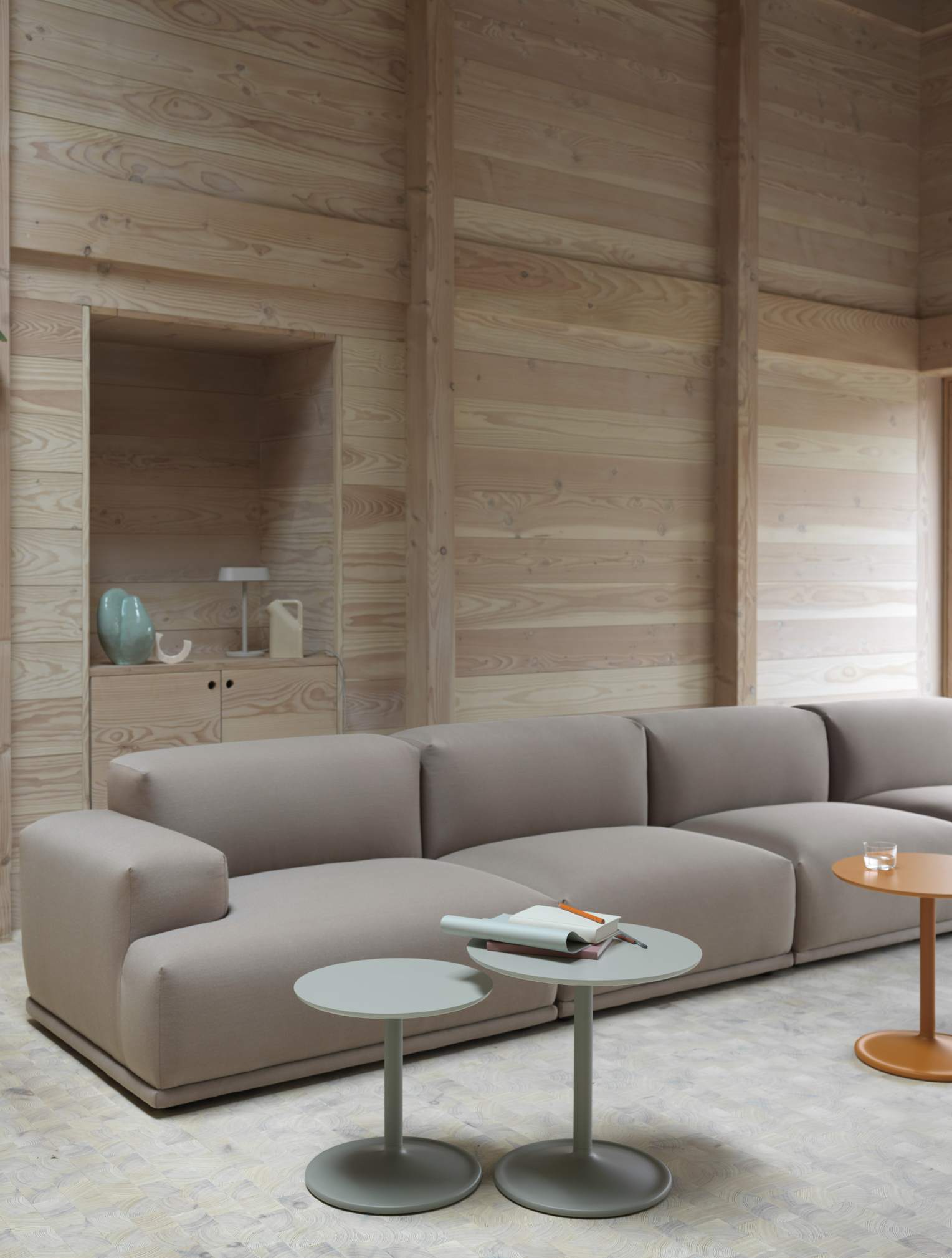 Muuto Soft Side Table Beistelltisch in Grau vor beigem Sofa und Holzwand, modernes Wohnzimmer Design.