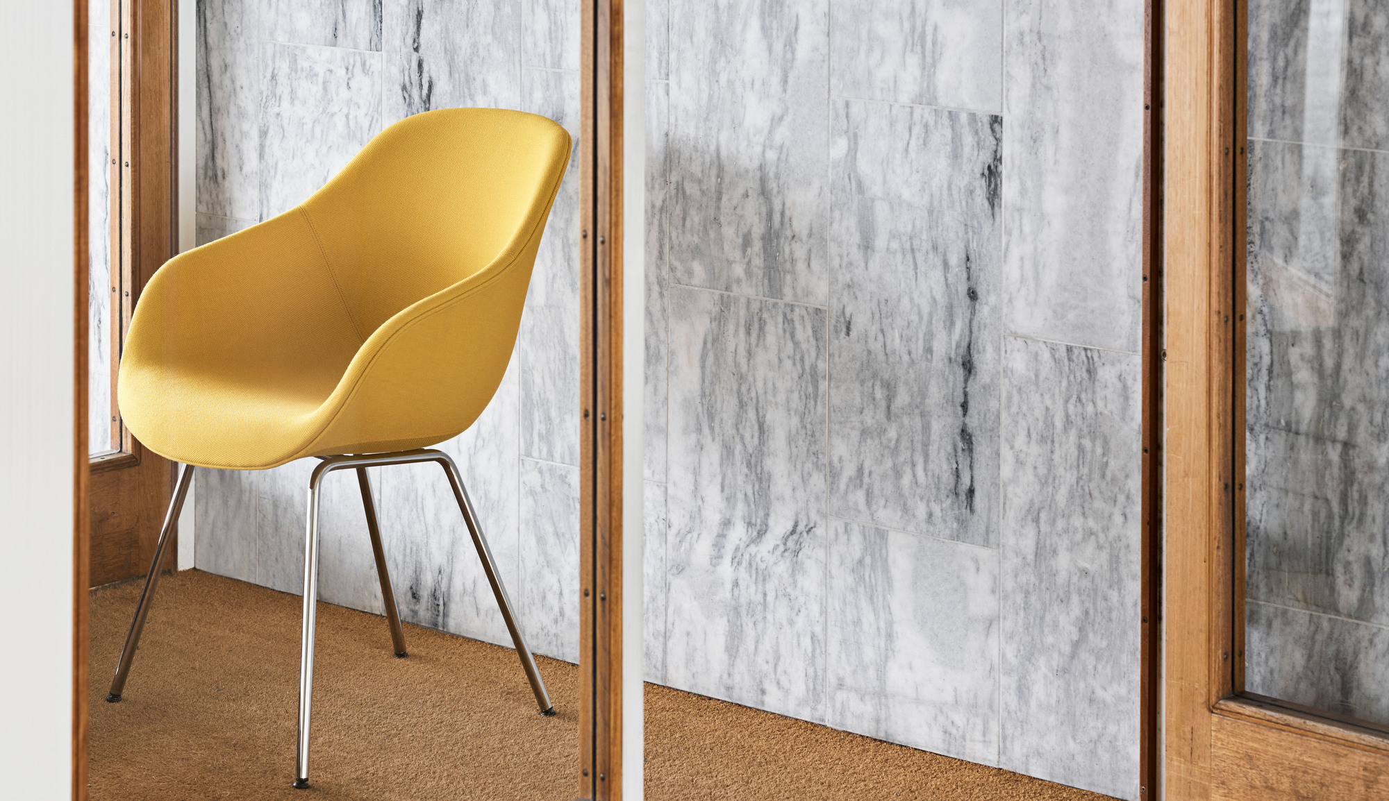 Gelber About a Chair AAC127 Stuhl von Hay mit verchromten Beinen vor Marmorwand.