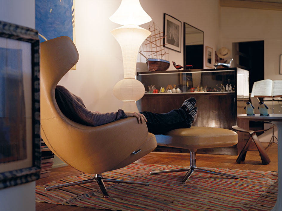Person entspannt im Vitra Grand Repos Sessel mit Ottoman in Cosy Fossil Farbe.