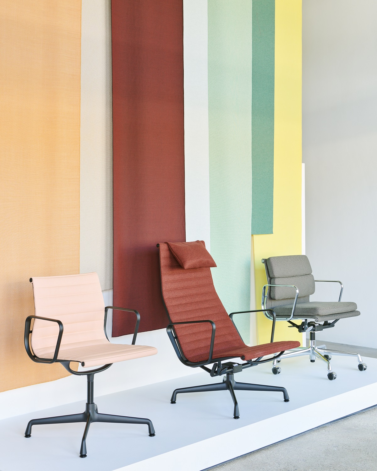 Drei Vitra Soft Pad Chairs EA217 in Beige, Rot und Grau vor farbigem Hintergrund.