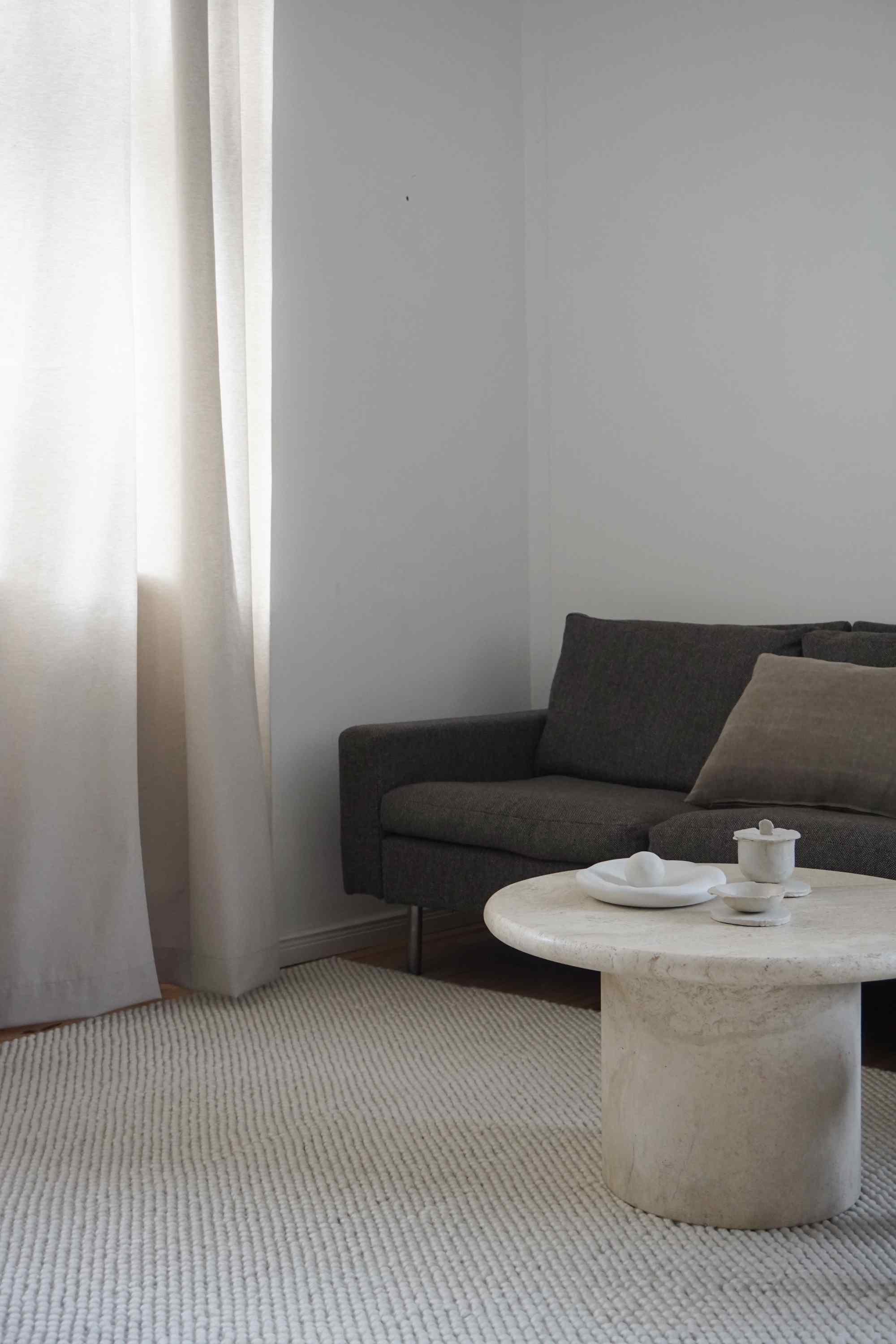 Off-white Tact Rug Teppich von Woud, 170x240 cm, in einem minimalistischen Wohnzimmer mit Sofa.