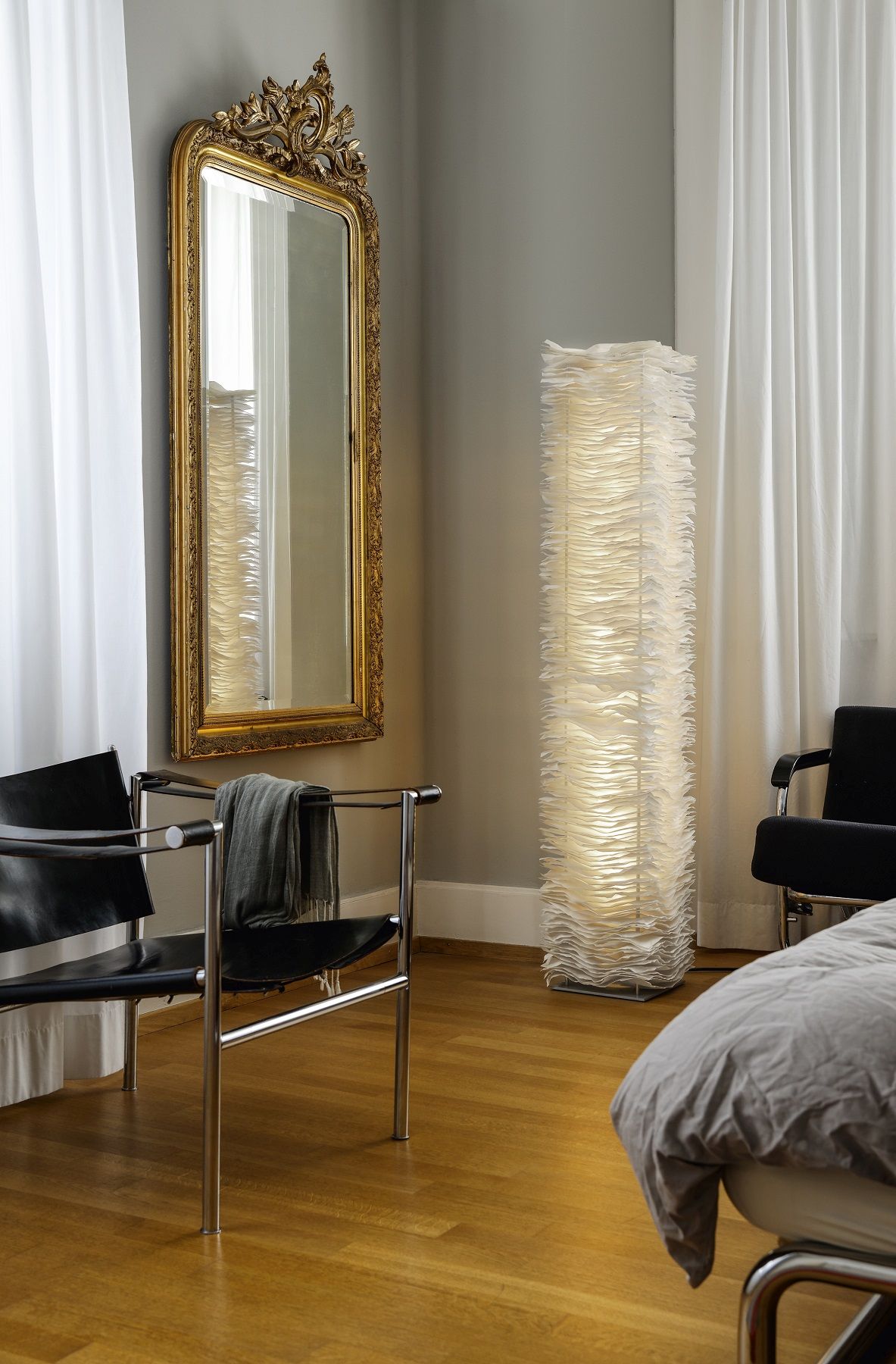 Elegante Stehlampe mit Papier-Design, goldener Spiegel und schwarzer Sessel im Schlafzimmer.