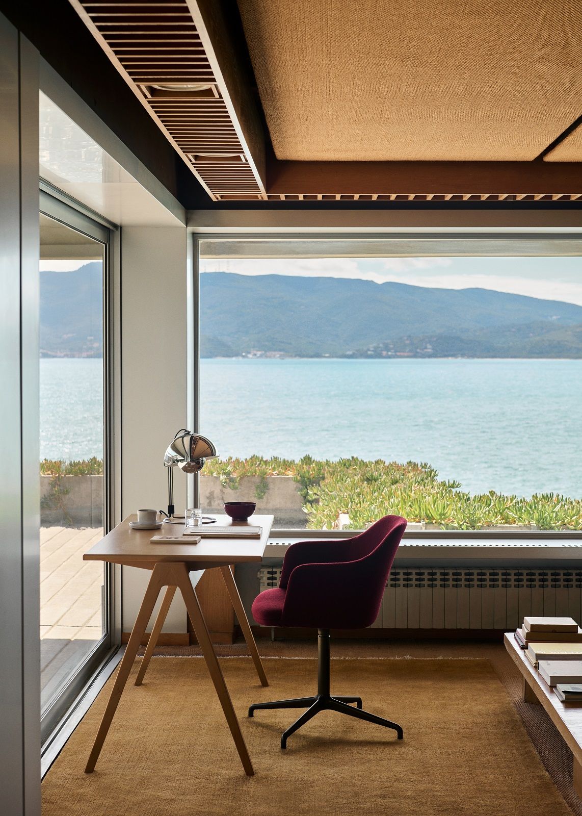 AndTradition Daystak Tisch mit Meerblick: Moderner Schreibtisch aus Holz mit rotem Bürostuhl in stilvollem Arbeitszimmer.