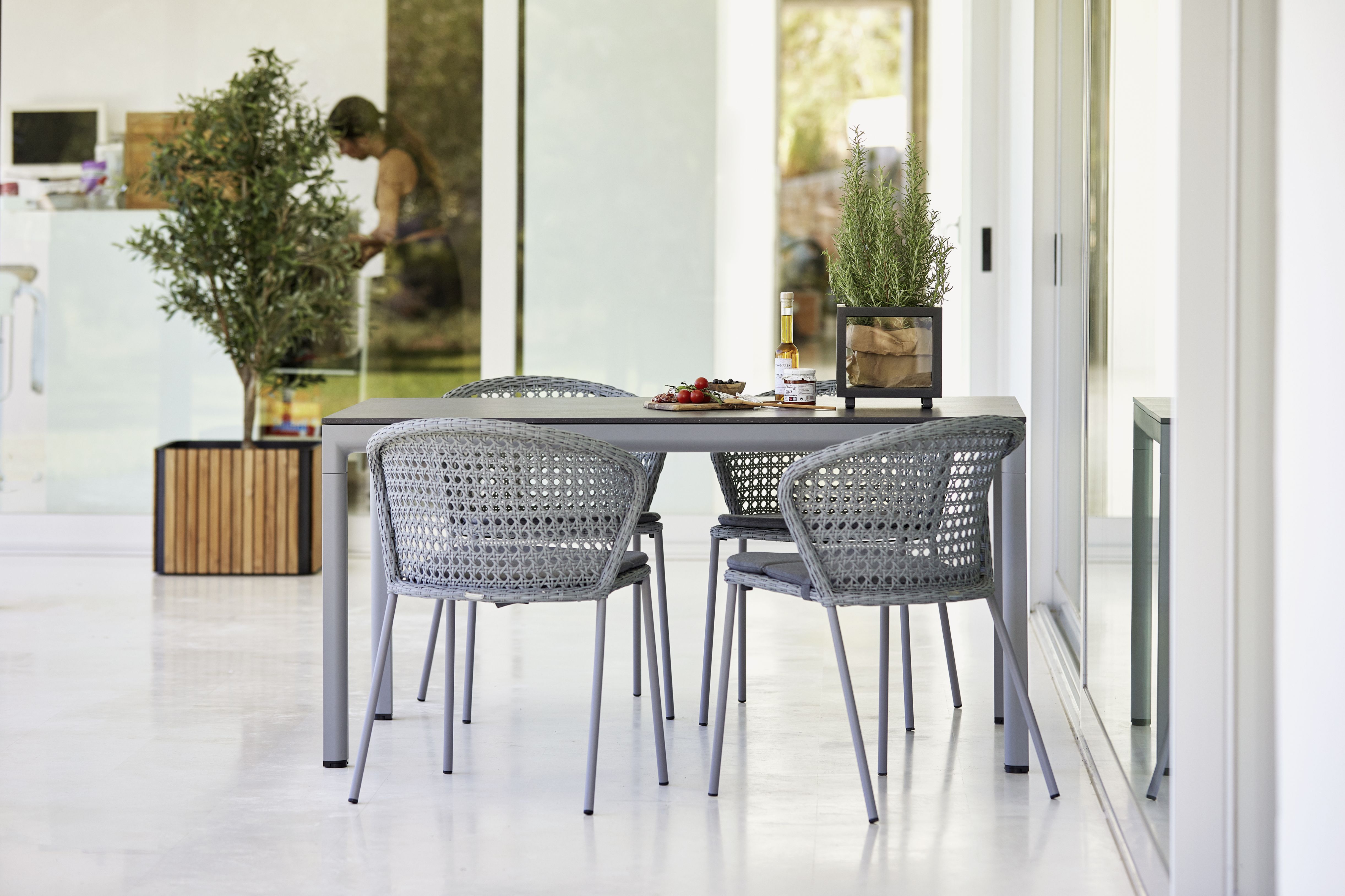Quadratischer Cane-Line Combine Pflanzkübel aus Teakholz mit Kräutern auf Esstisch mit Rattan-Stühlen.