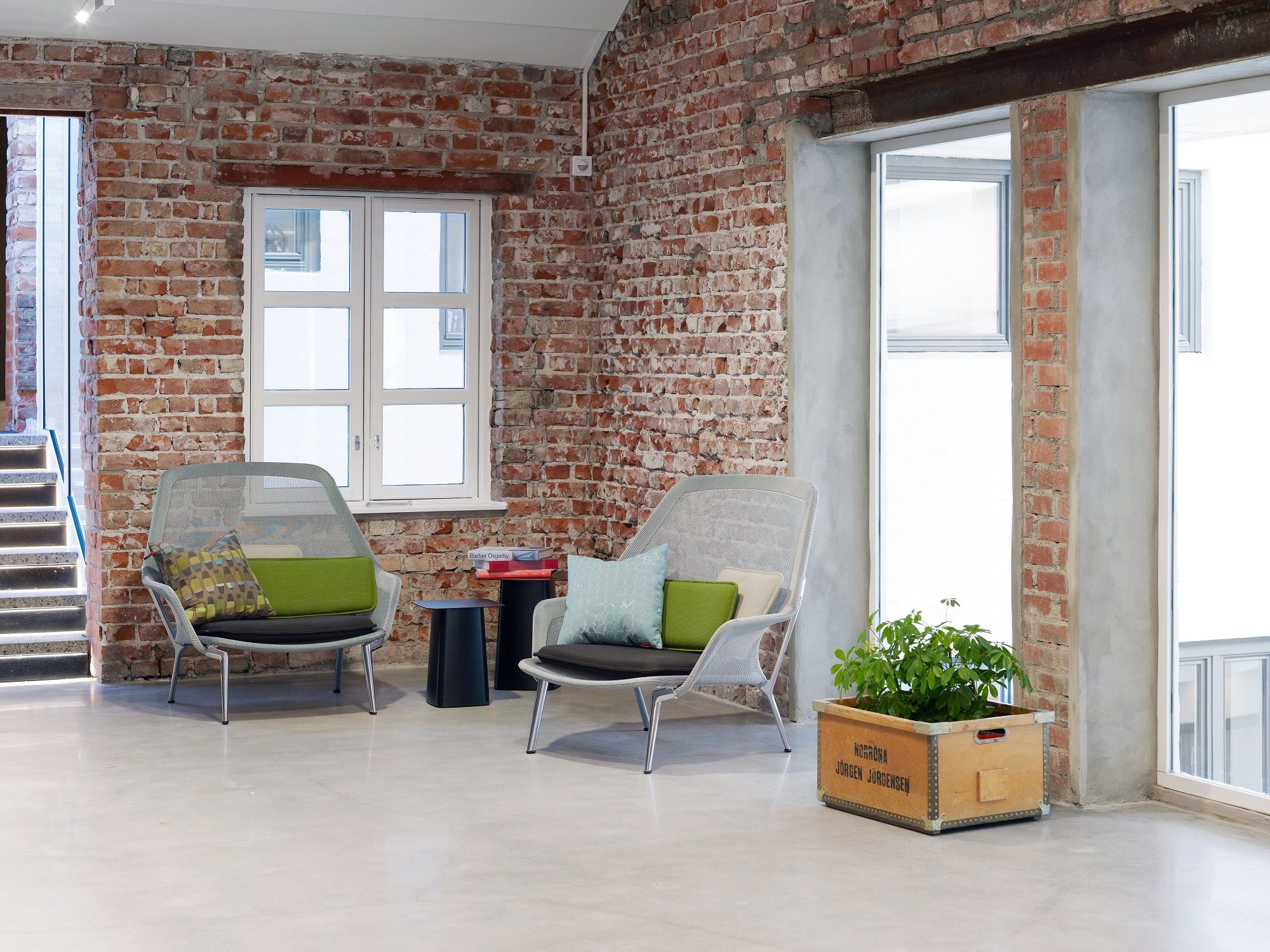 Zwei graue Slow Chair Sessel von Vitra in einem Raum mit Backsteinwand und Betonboden.