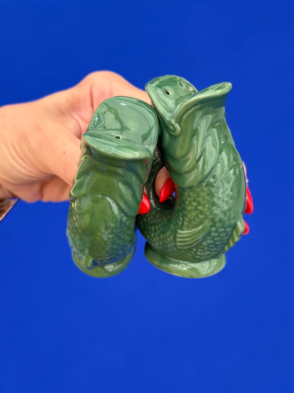 Grüne Gluggle Fisch Salz- und Pfefferstreuer im Detail, gehalten von einer Hand vor blauem Hintergrund.