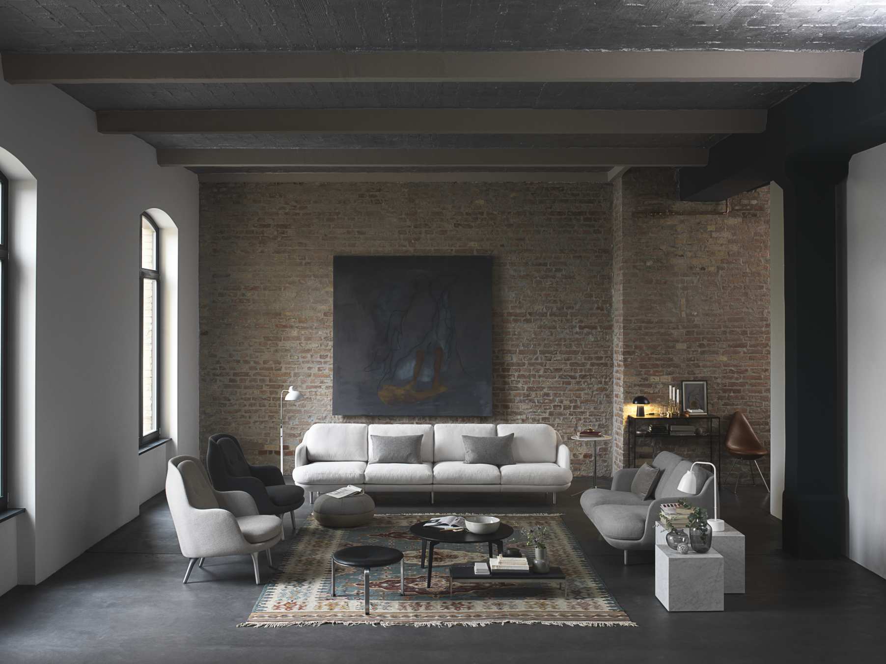 Heller Wohnraum mit PK62 Couchtisch von Fritz Hansen, Teppich, Sofa und Sesseln vor einer Backsteinwand.