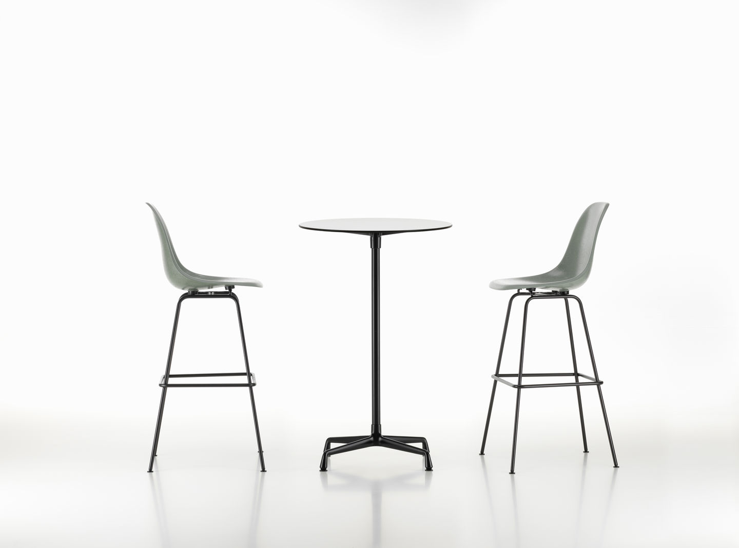Zwei Eames Plastic Bar Stools von Vitra mit schwarzem Gestell und einem runden Tisch.