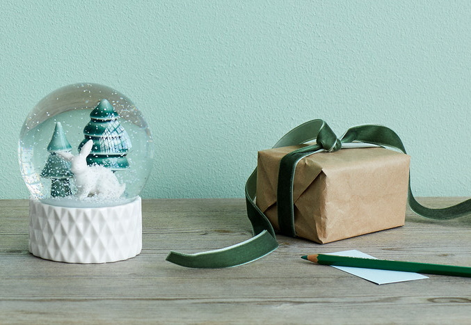 Schneekugel mit Hase und Tannenbäumen, Geschenk mit Schleife und Stift auf Holztisch.