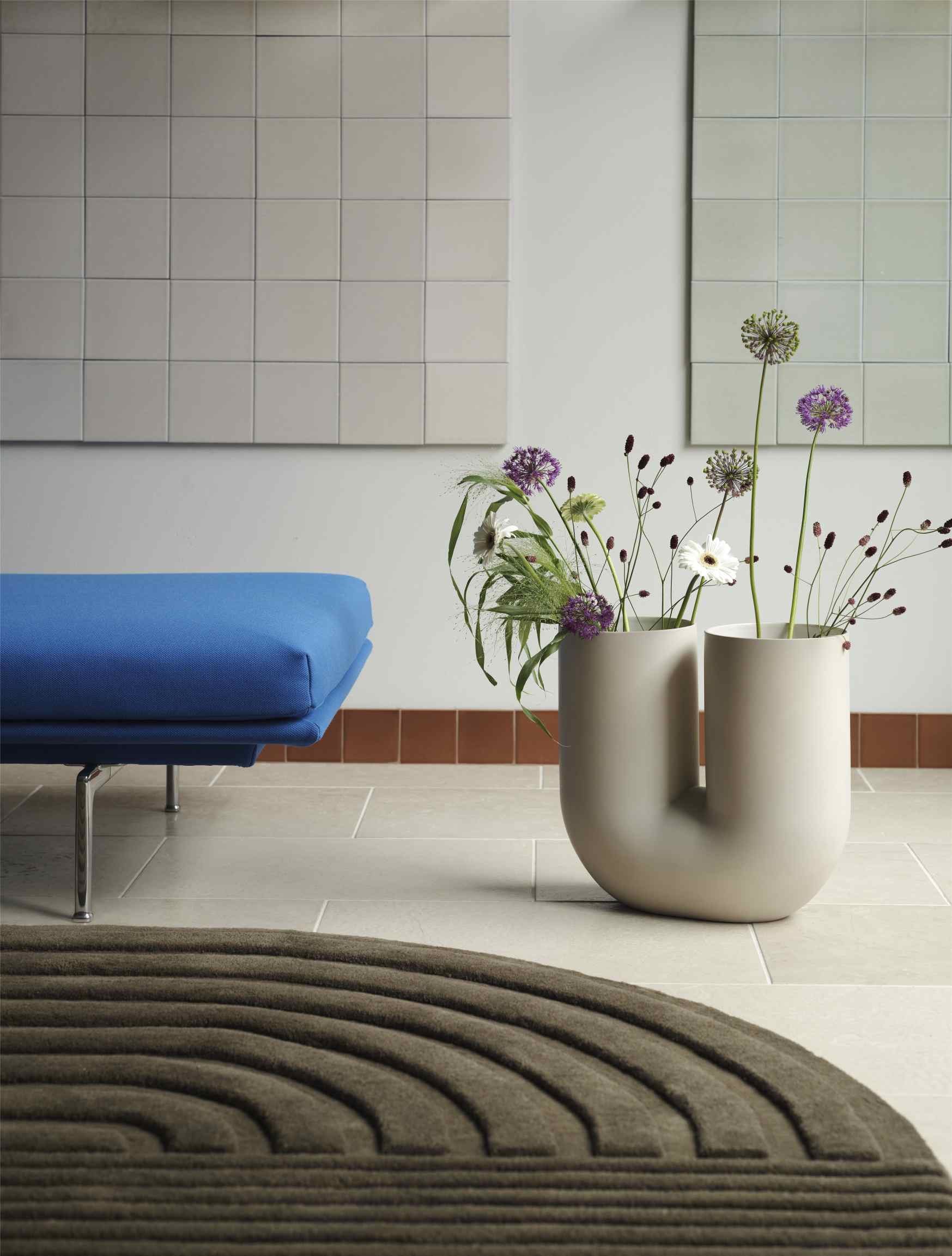 Nahaufnahme der Muuto Kink Vase Sand H 39 cm mit Blumen, stilvolle Wohnzimmerdekoration mit Teppich und Sofa.