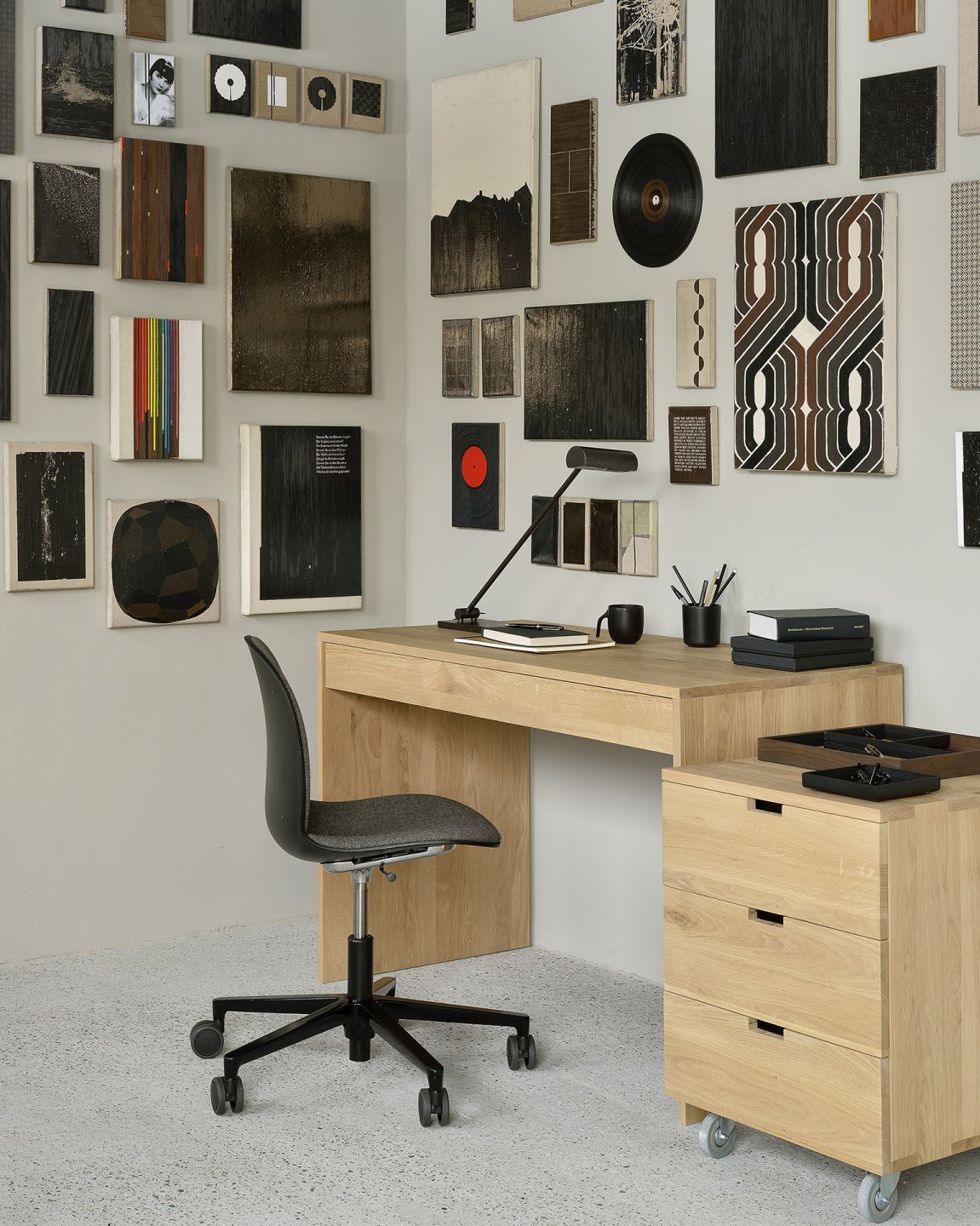 Ethnicraft Wave Schreibtisch aus Eiche mit Rollcontainer und Bürostuhl vor einer Wand voller Kunst.