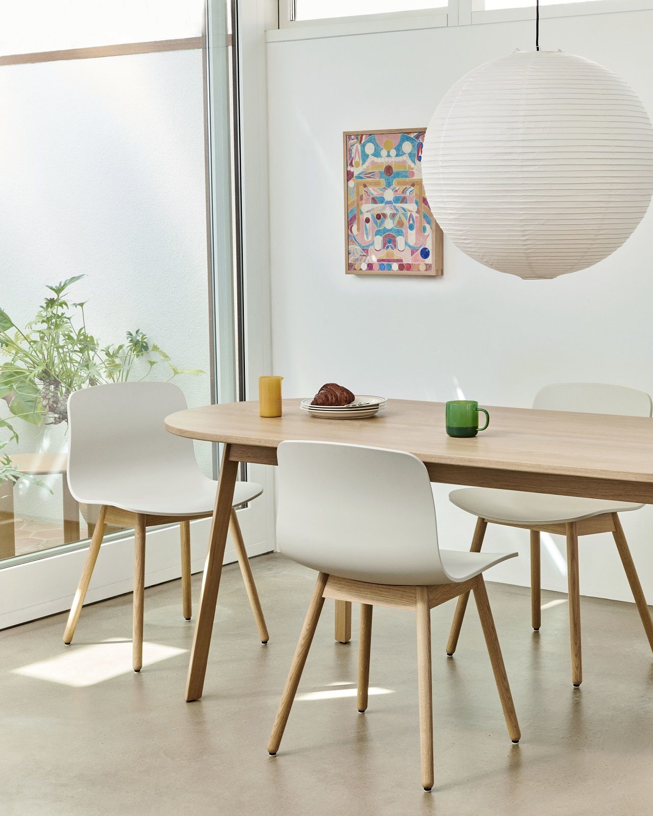 Heller Essbereich mit ovalem Hay Triangle Leg Table Esstisch aus Eichenholz und weißen Stühlen.