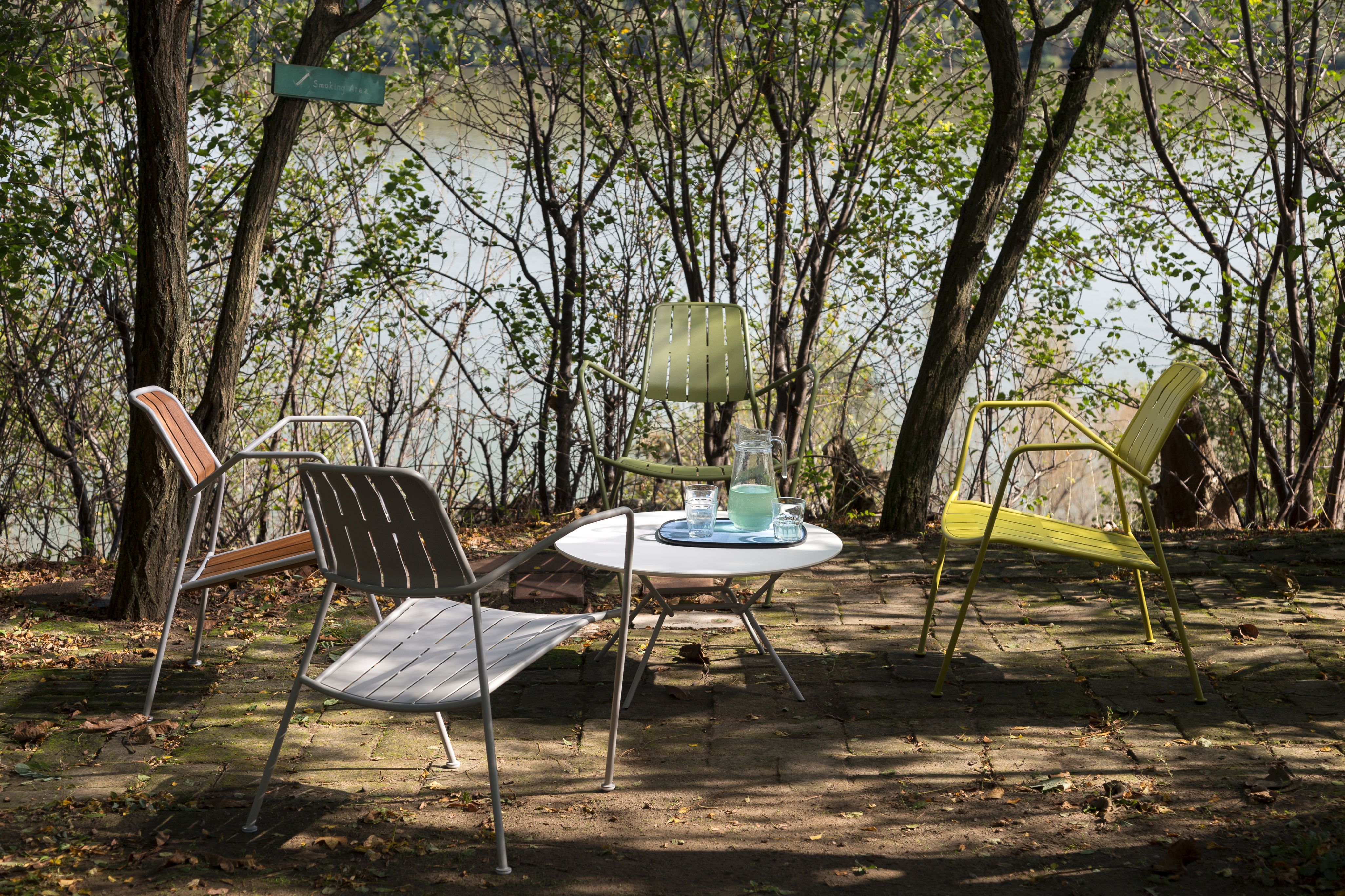 Mehrere Prostoria Osmo Outdoor Stühle in verschiedenen Farben um einen Tisch im Garten.