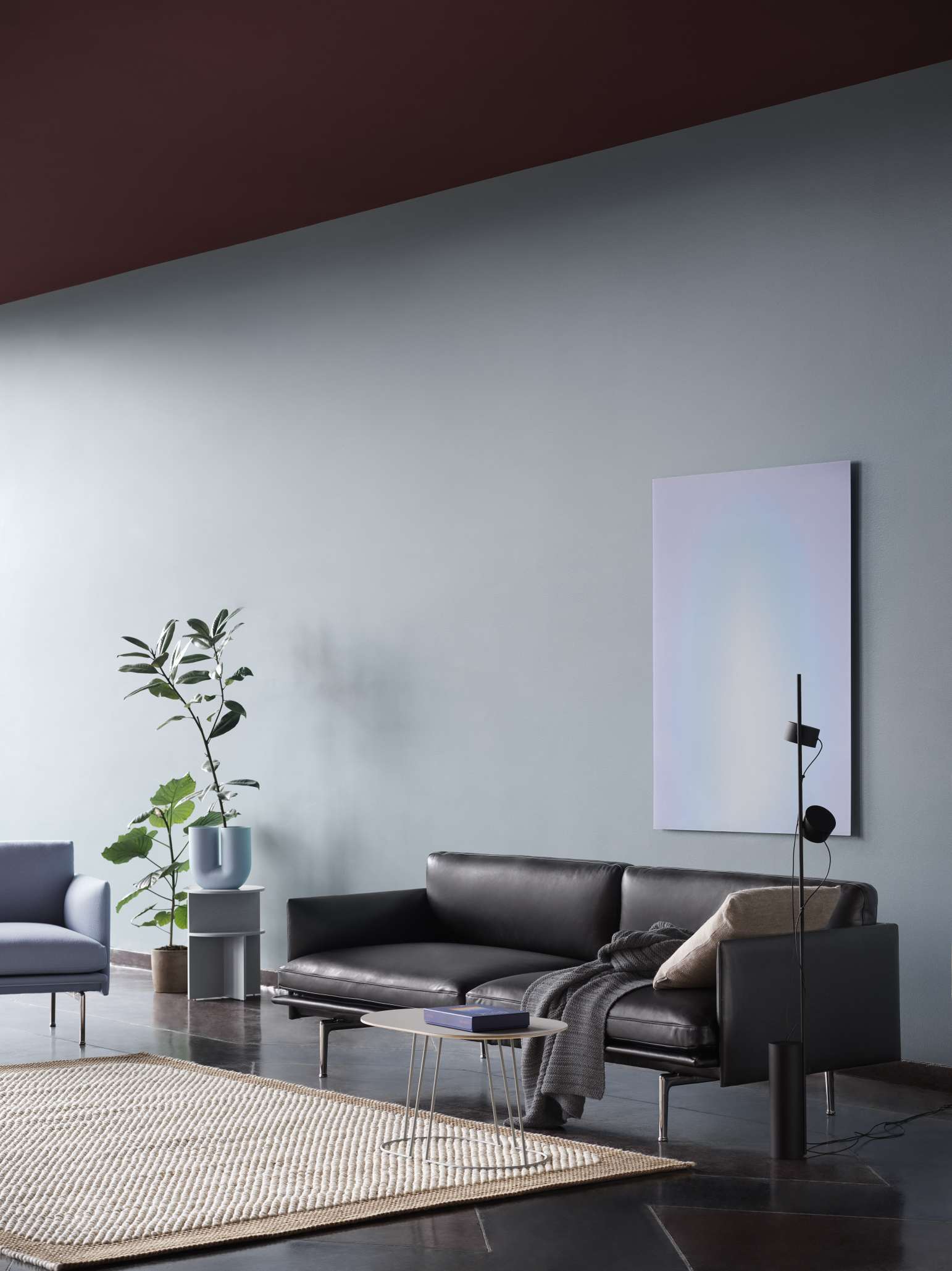 Wohnzimmer-Szene mit dunklem Ledersofa und grauer Ample Throw Decke von Muuto.