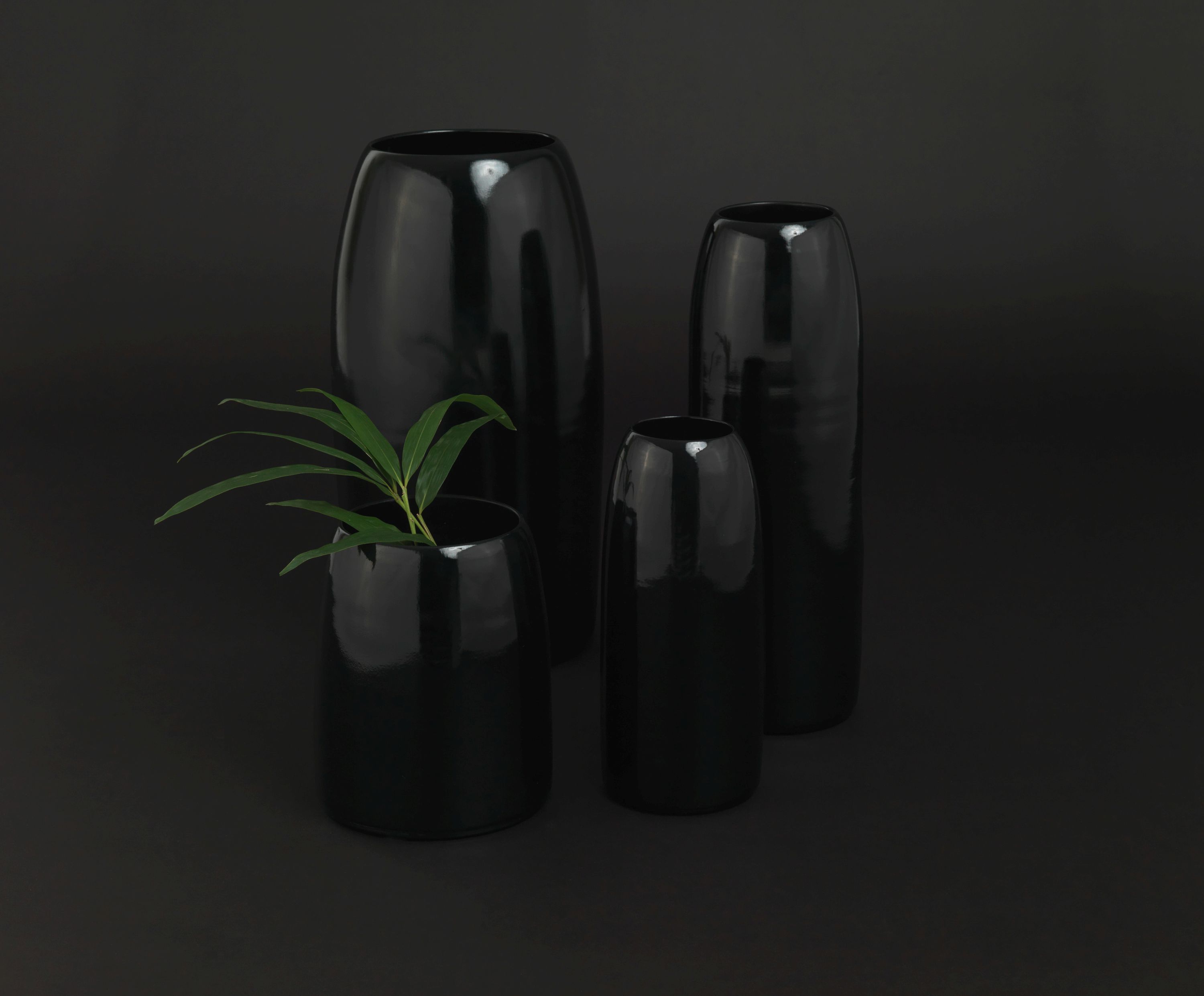 Schönbuch Carla Vase L, ein Set aus vier eleganten, glänzenden, schwarzen Design Vasen auf dunklem Hintergrund.