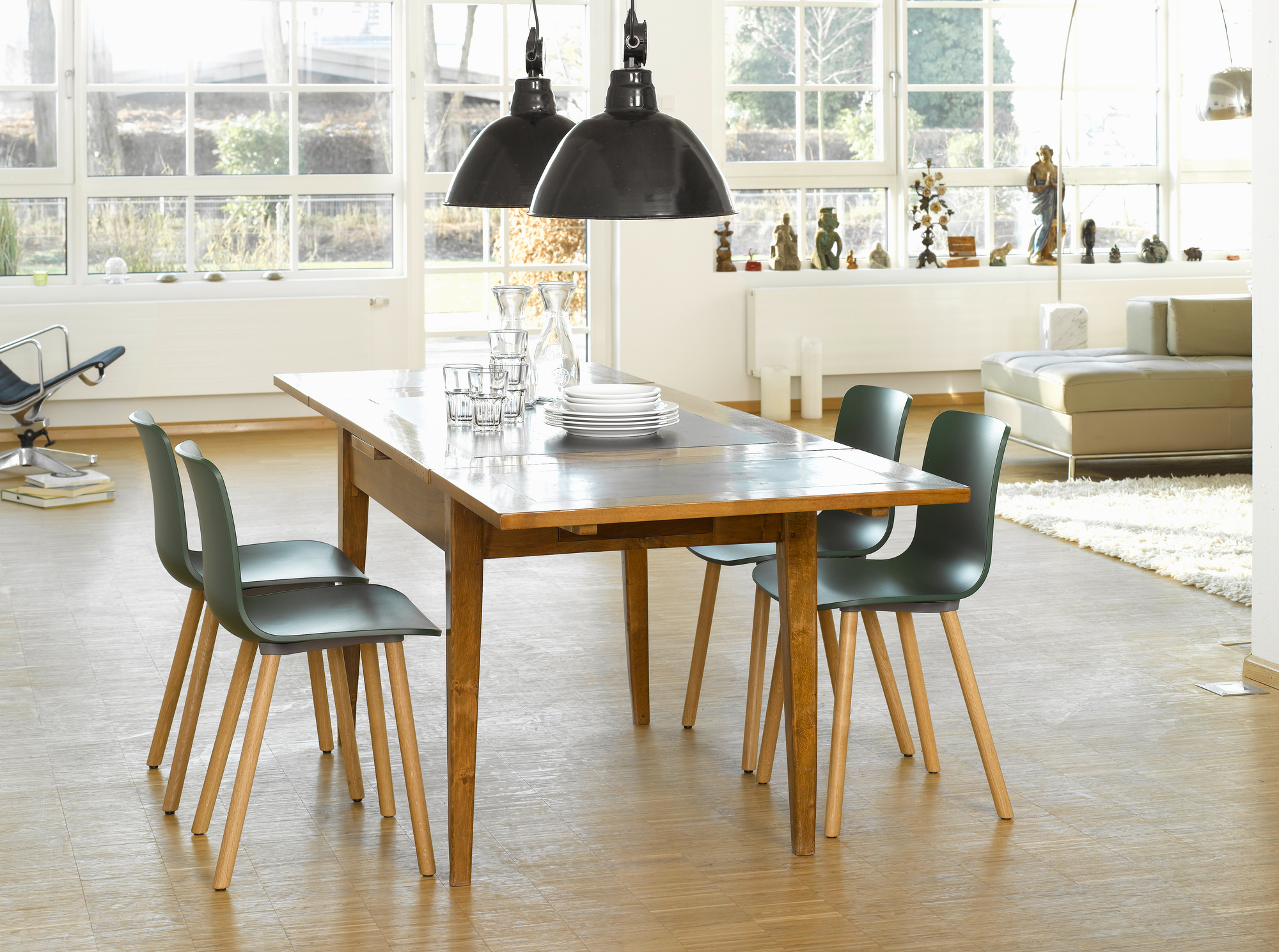 Esszimmer mit Holztisch, Geschirr und vier grünen Vitra Hal Ply Wood Stühlen mit Holzbeinen.
