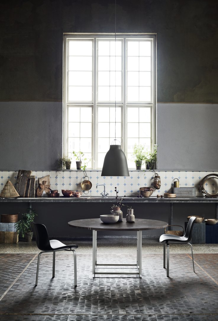 Graue Caravaggio Pendelleuchte von Fritz Hansen über Esstisch in stilvollem Interieur mit Küchenelementen.