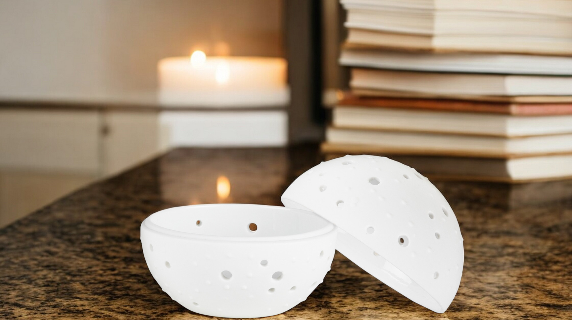 Living Wunderkugel: Weiße Duftlampe/Aromalampe mit Punktmuster, geöffnet auf Tisch mit Kerze und Büchern im Hintergrund.