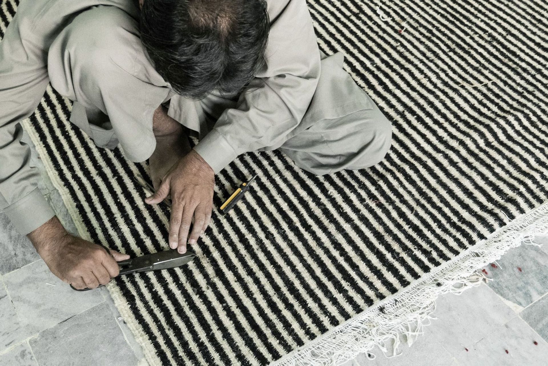 Handwerker schneidet Fransen an einem handgeknüpften Teppich mit schwarzen und weißen Streifen. Hochwertiger Wollteppich.