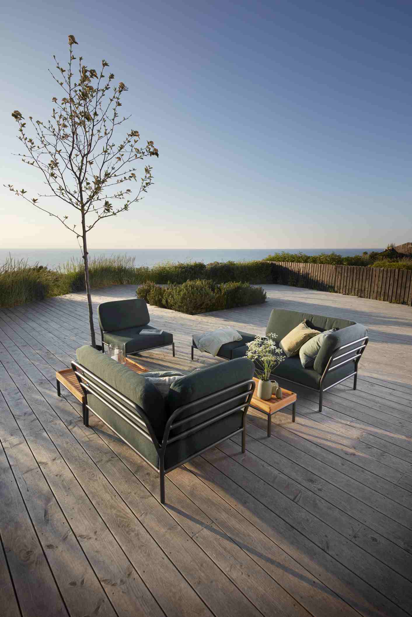 Houe Level Outdoor Sofa und Sessel auf Holzterrasse mit Meerblick. Gartenmöbel für entspannte Stunden.