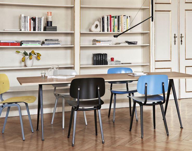 Esstisch mit mehreren Revolt Chair Stühlen von Hay in verschiedenen Farben vor einem Bücherregal.
