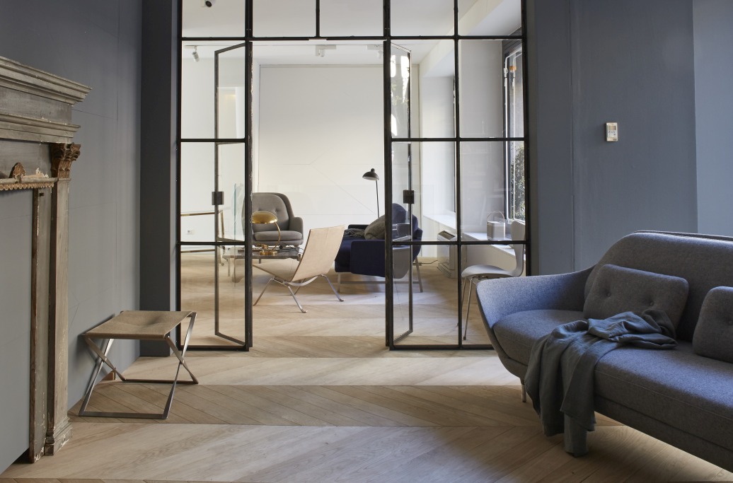 PK91 Falthocker von Fritz Hansen in stilvollem Wohnambiente, minimalistisches Design mit Metallgestell und hellem Stoffbezug.
