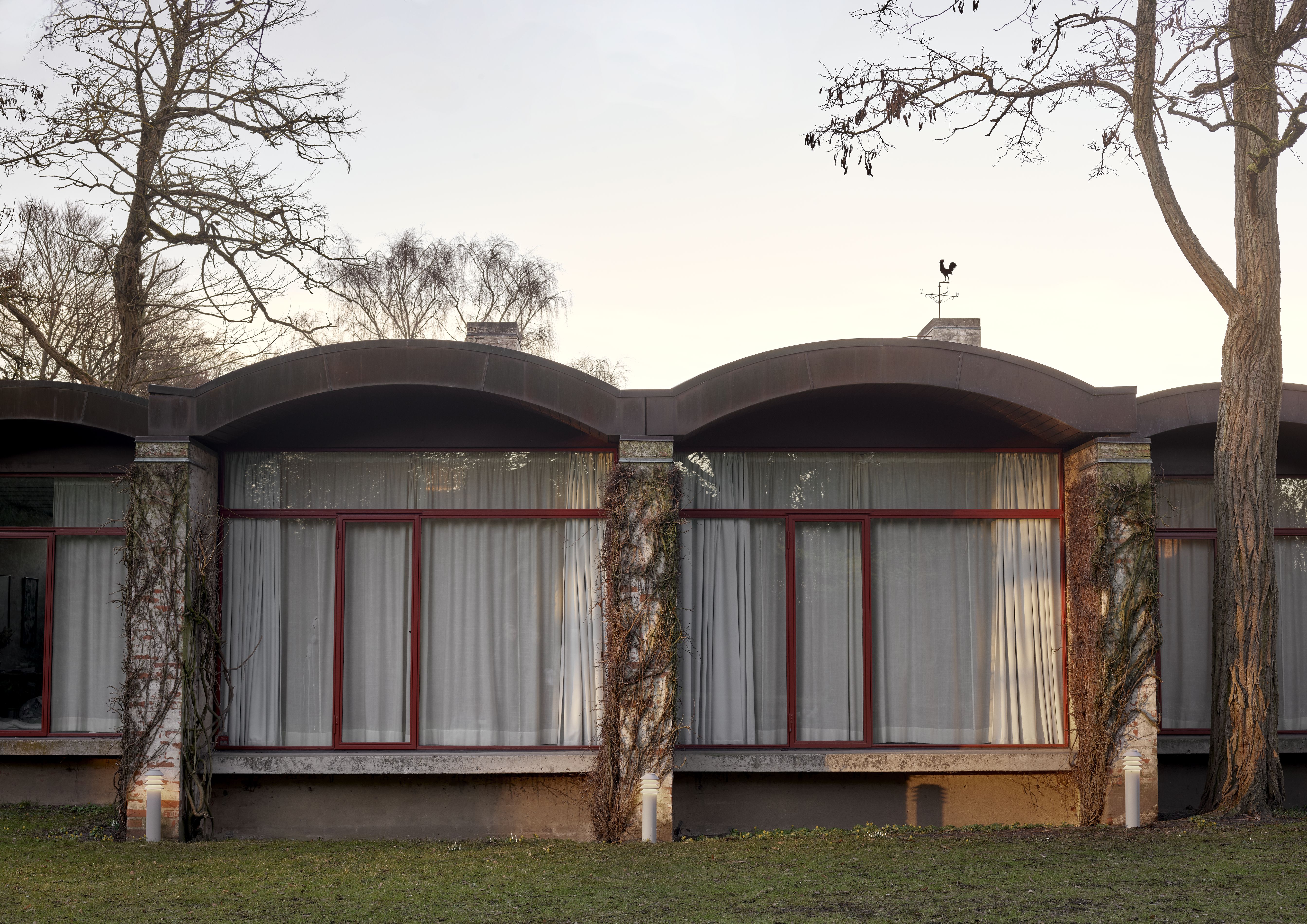 Bysted Garden Pollerleuchte von Louis Poulsen vor einem modernen Haus mit großen Fenstern und Bäumen.