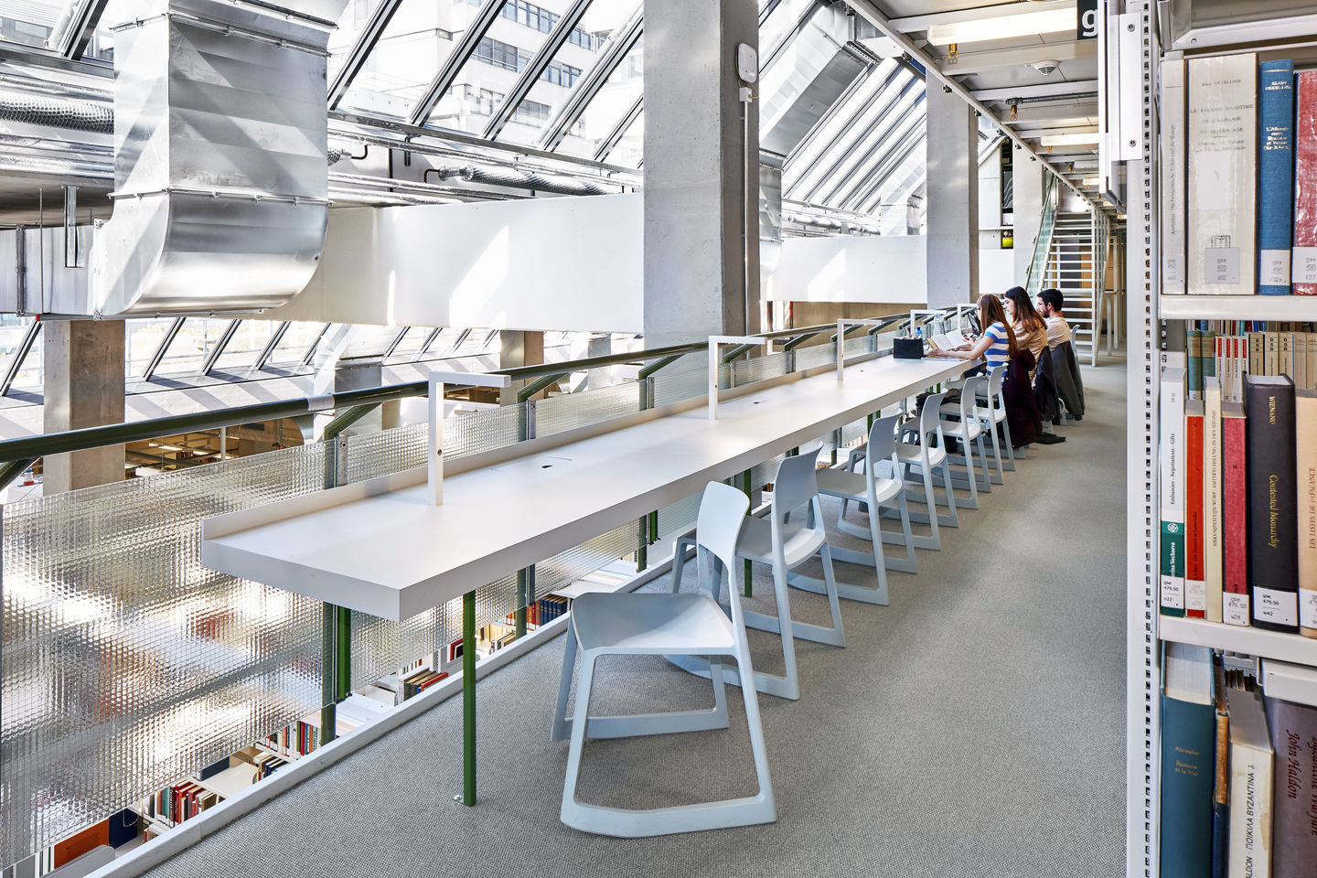 Helle Bibliothek mit langer Tischreihe und mehreren weißen Vitra Tip Ton Stühlen aus Kunststoff.